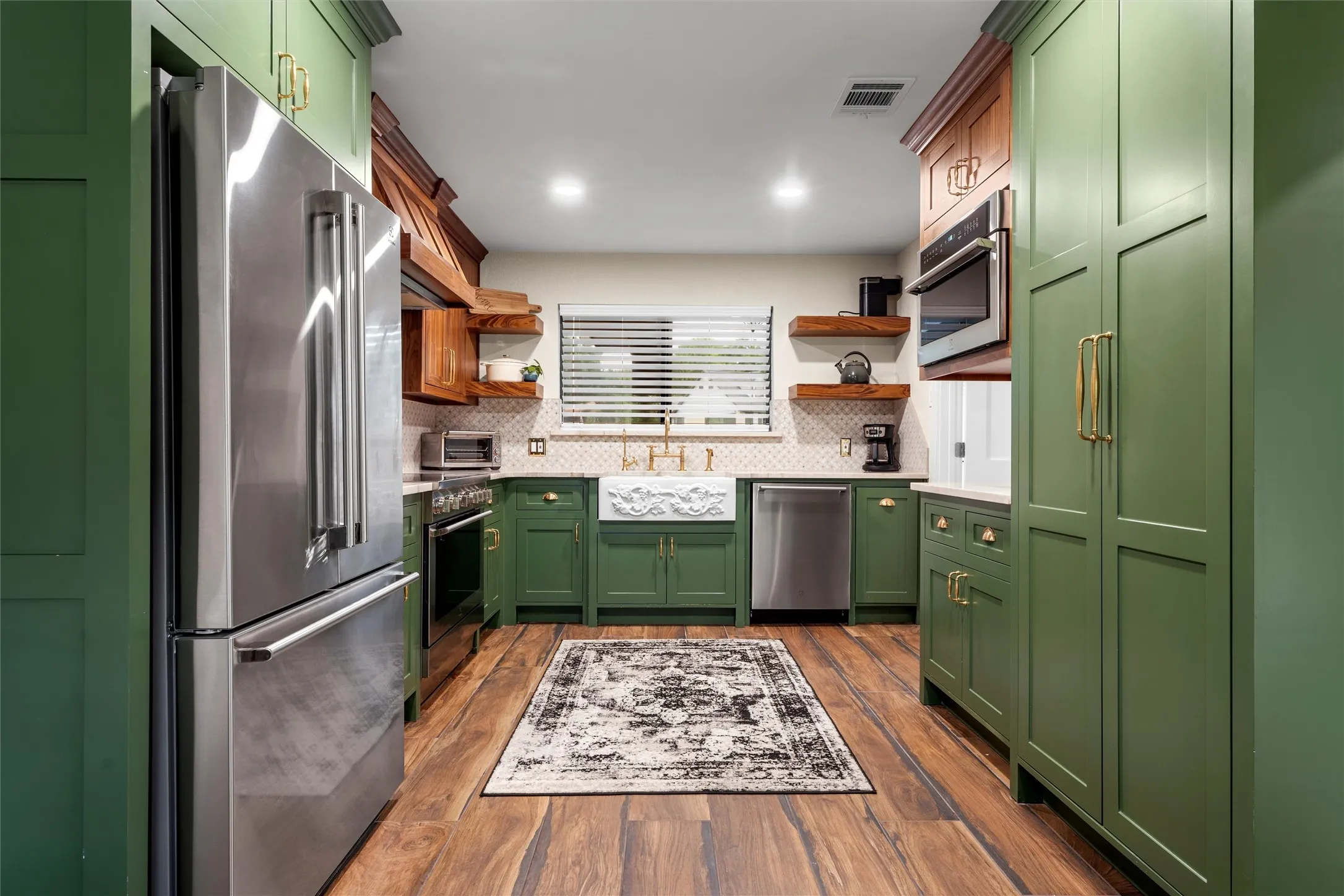 Modern kitchen featuring green shaker-style cabinetry, stainless steel appliances, wood-finish flooring, a farmhouse sink, and a tiled backsplash