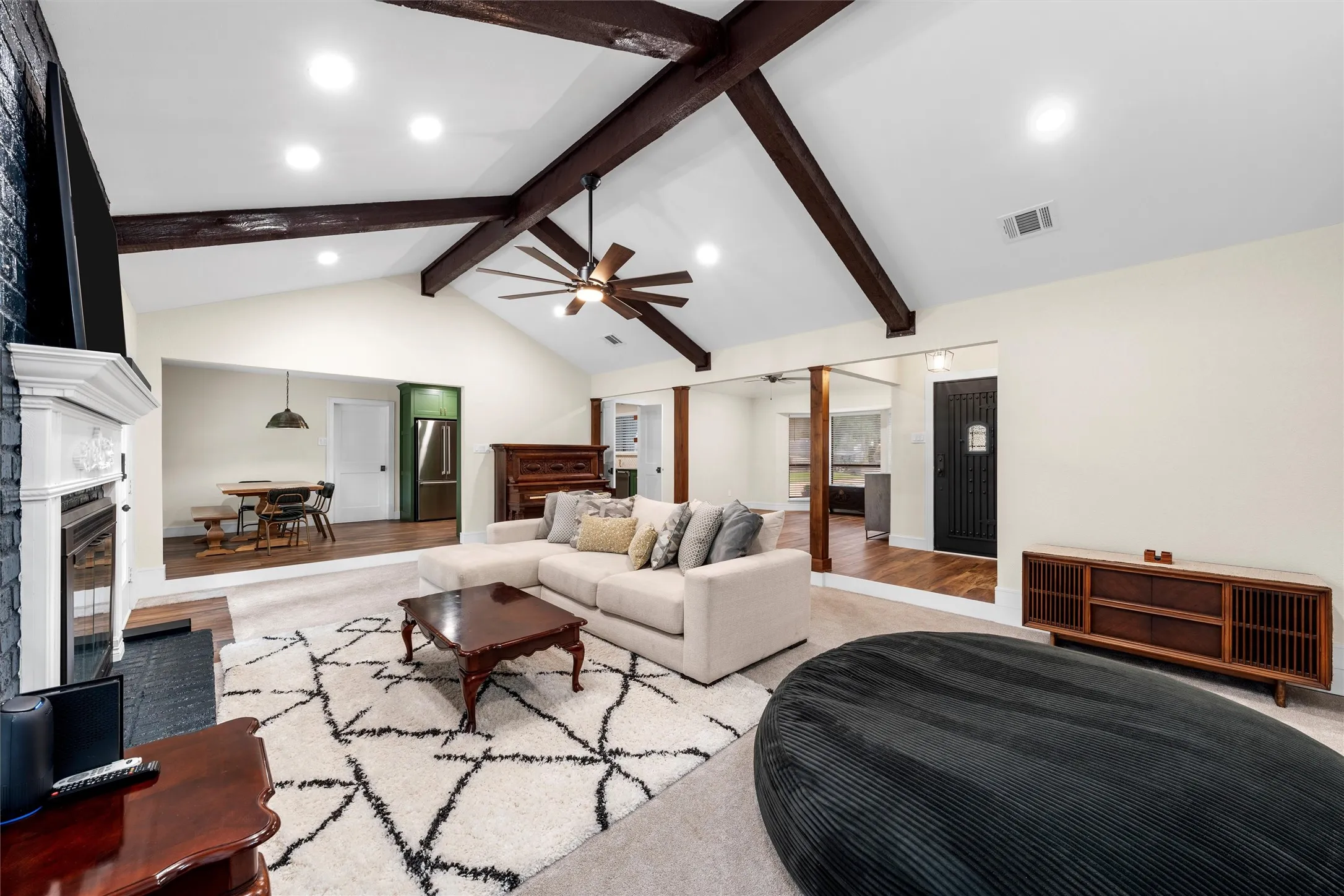 Spacious living area featuring a vaulted ceiling with exposed wood beams, recessed lighting, and a ceiling fan