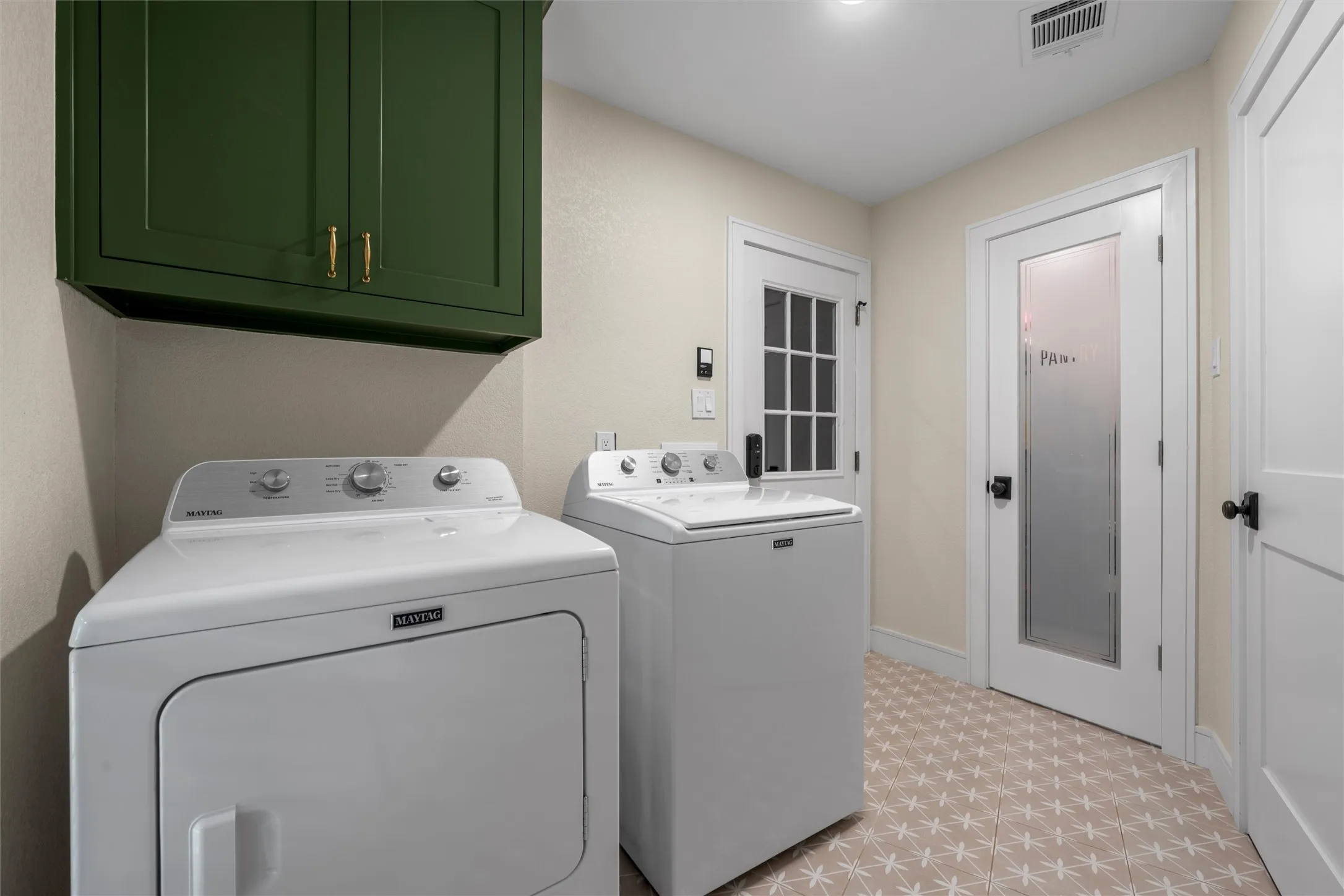 Laundry room featuring dark green cabinetry with brass hardware, patterned floor tile, and white doors with dark hardware