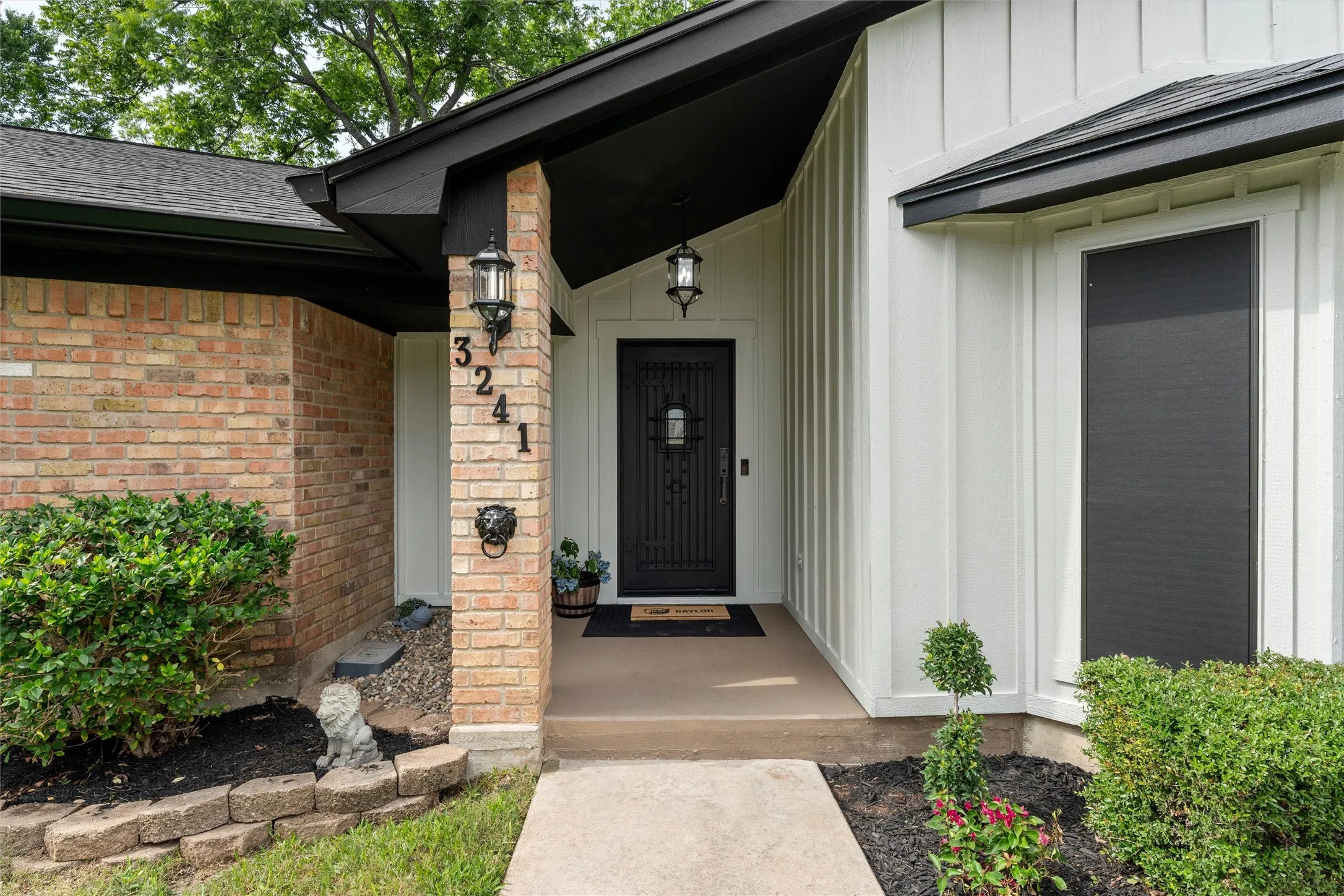 Entryway featuring a black wrought iron door, brick facade, board-and-batten siding, and exterior sconces