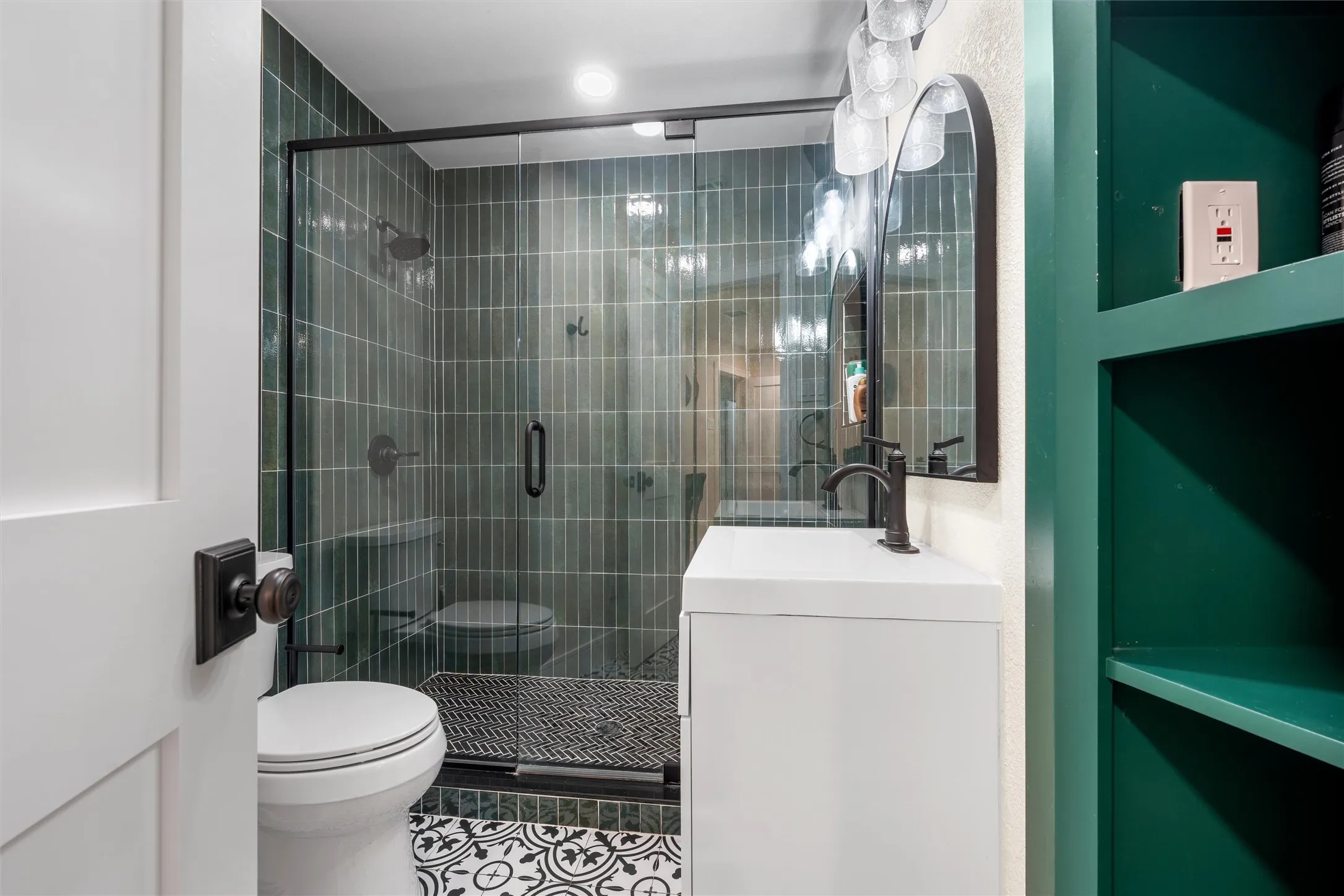 Bathroom featuring a glass-enclosed shower with vertical tiled walls, a white vanity with a matte black faucet, and patterned floor tiles