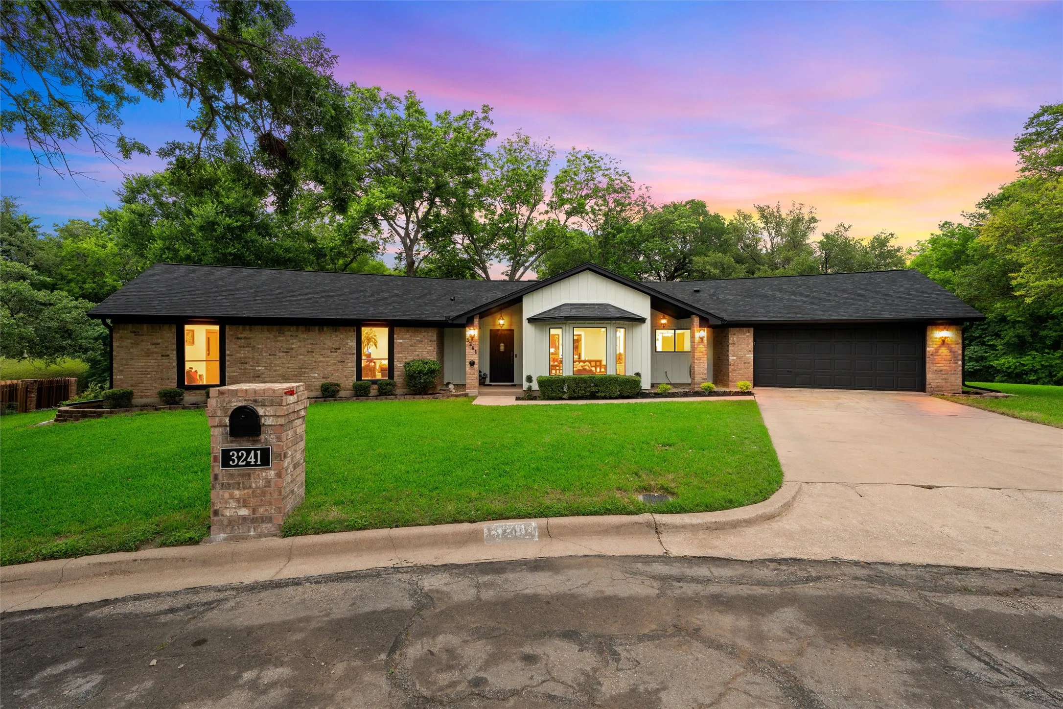 Brick and siding exterior featuring a prominent two-car garage, manicured lawn, and mature trees
