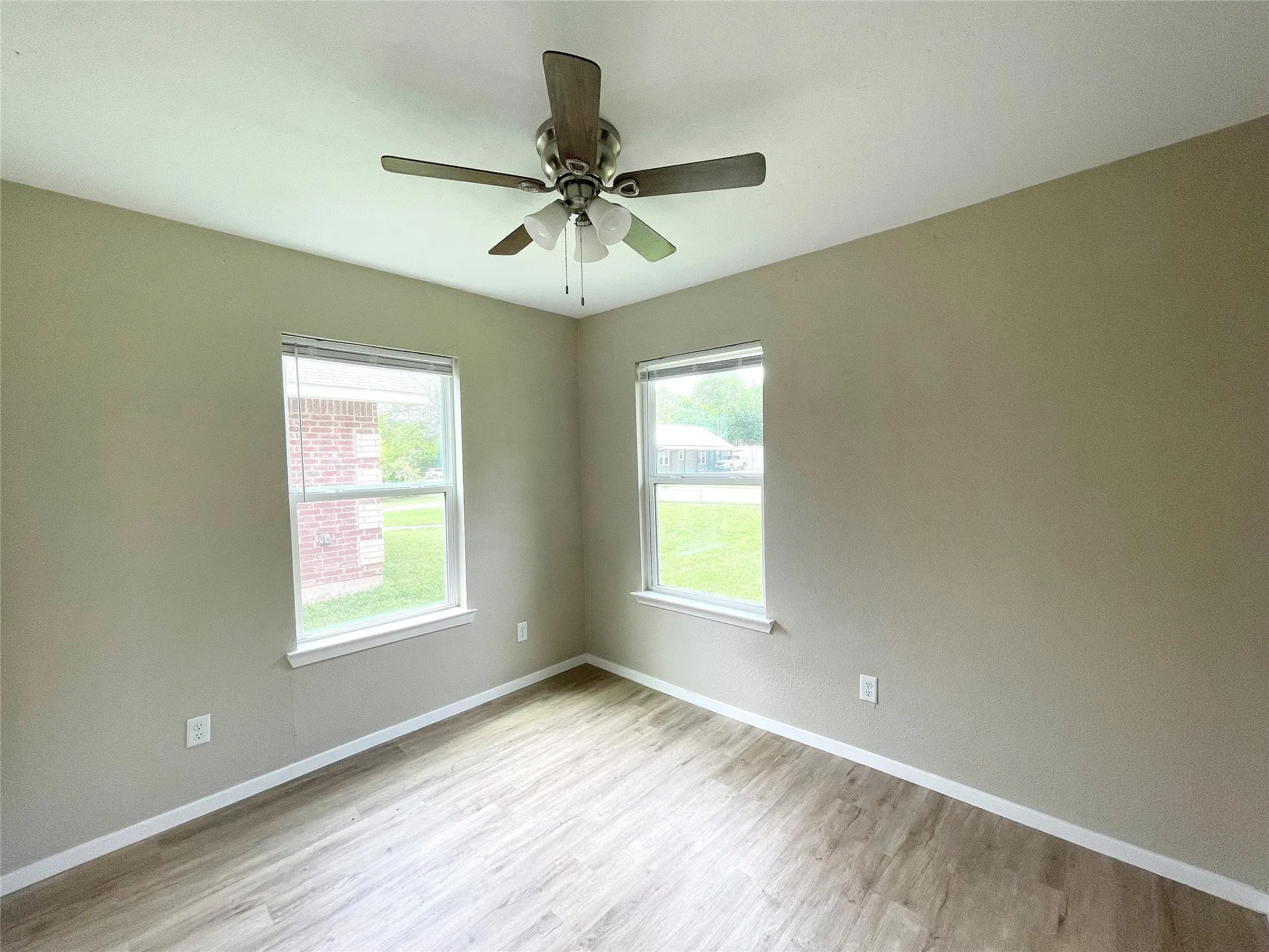 Room featuring light wood-finish flooring, two large windows, a ceiling fan with integrated lighting, neutral wall tones, and white trim