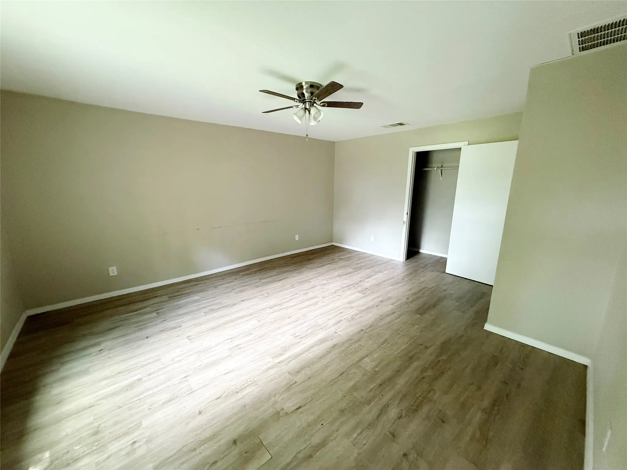Spacious room featuring light-toned wood-finish flooring, neutral wall paint, white baseboards, and a ceiling fan