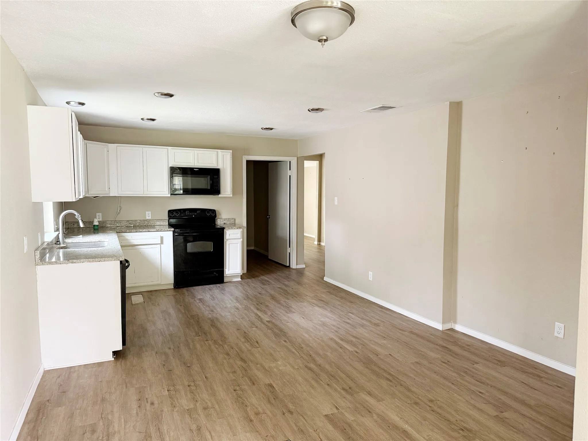 Open-concept kitchen and living area featuring wood-finish flooring, white cabinetry, granite-style countertops, and recessed lighting