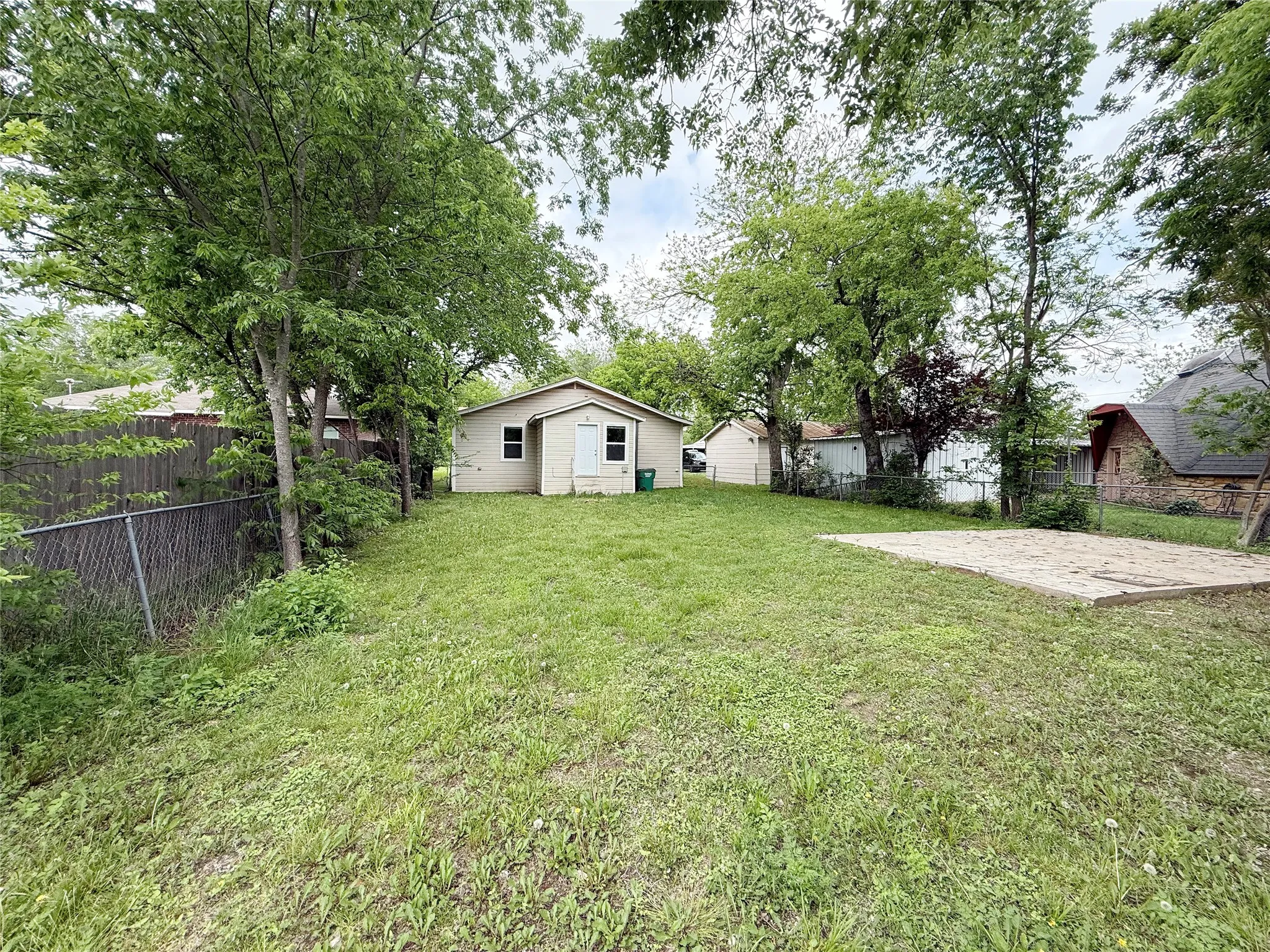 Expansive backyard featuring a manicured lawn, mature trees, and a concrete patio