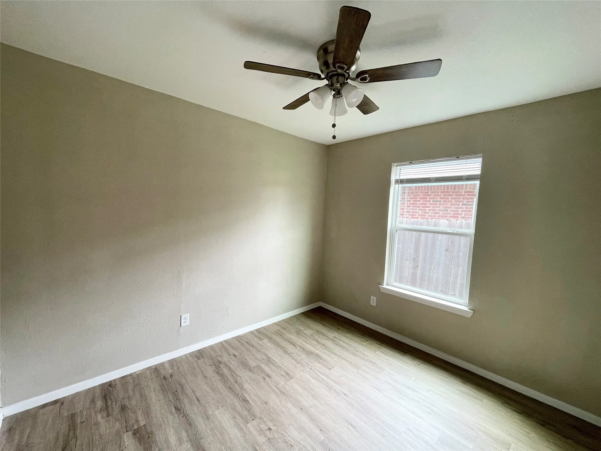 Room featuring wood-finish flooring, a ceiling fan with light fixture, and a single window with blinds