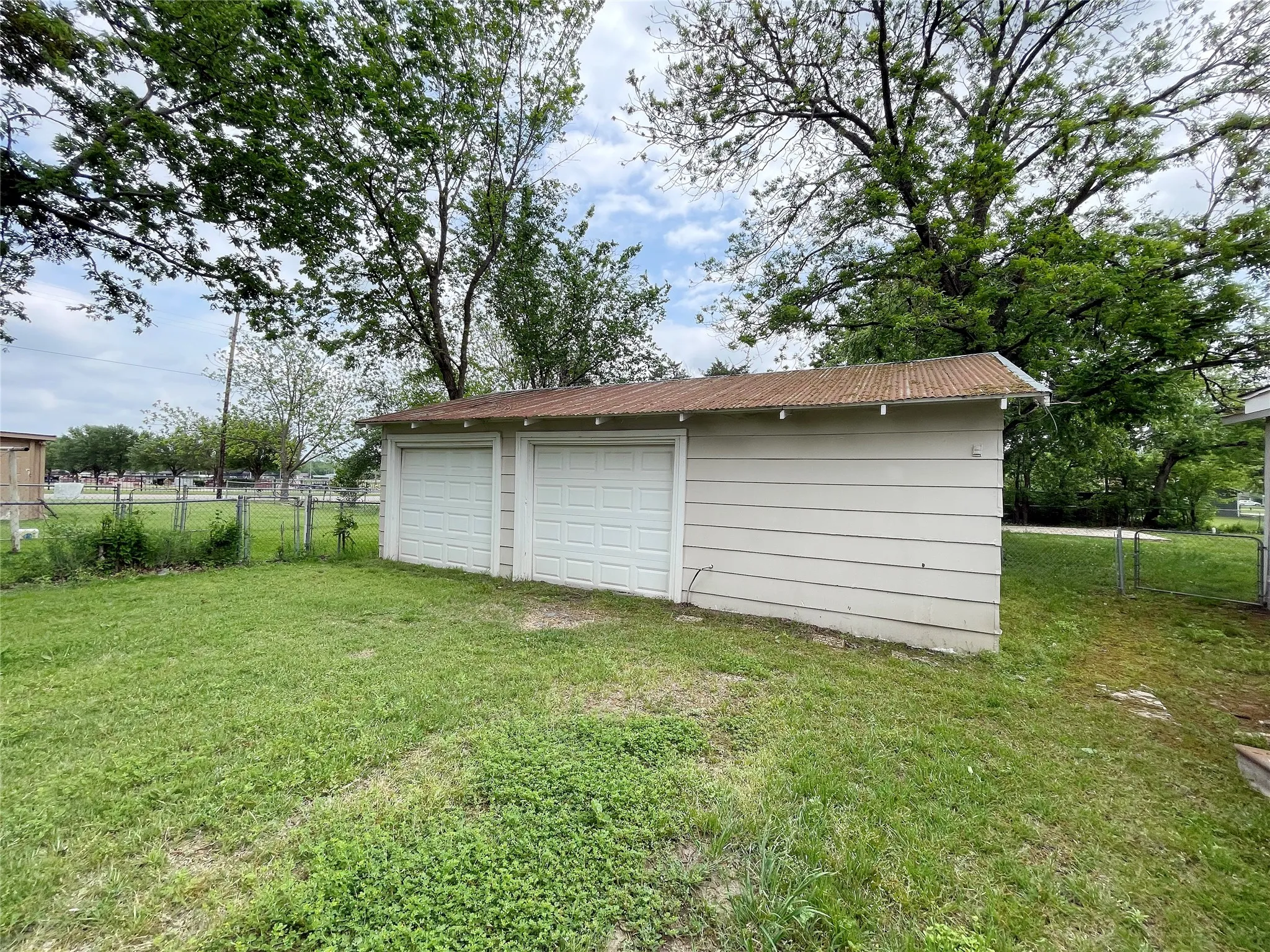 Detached two-car garage with white paneled garage doors, horizontal siding, and a corrugated metal roof