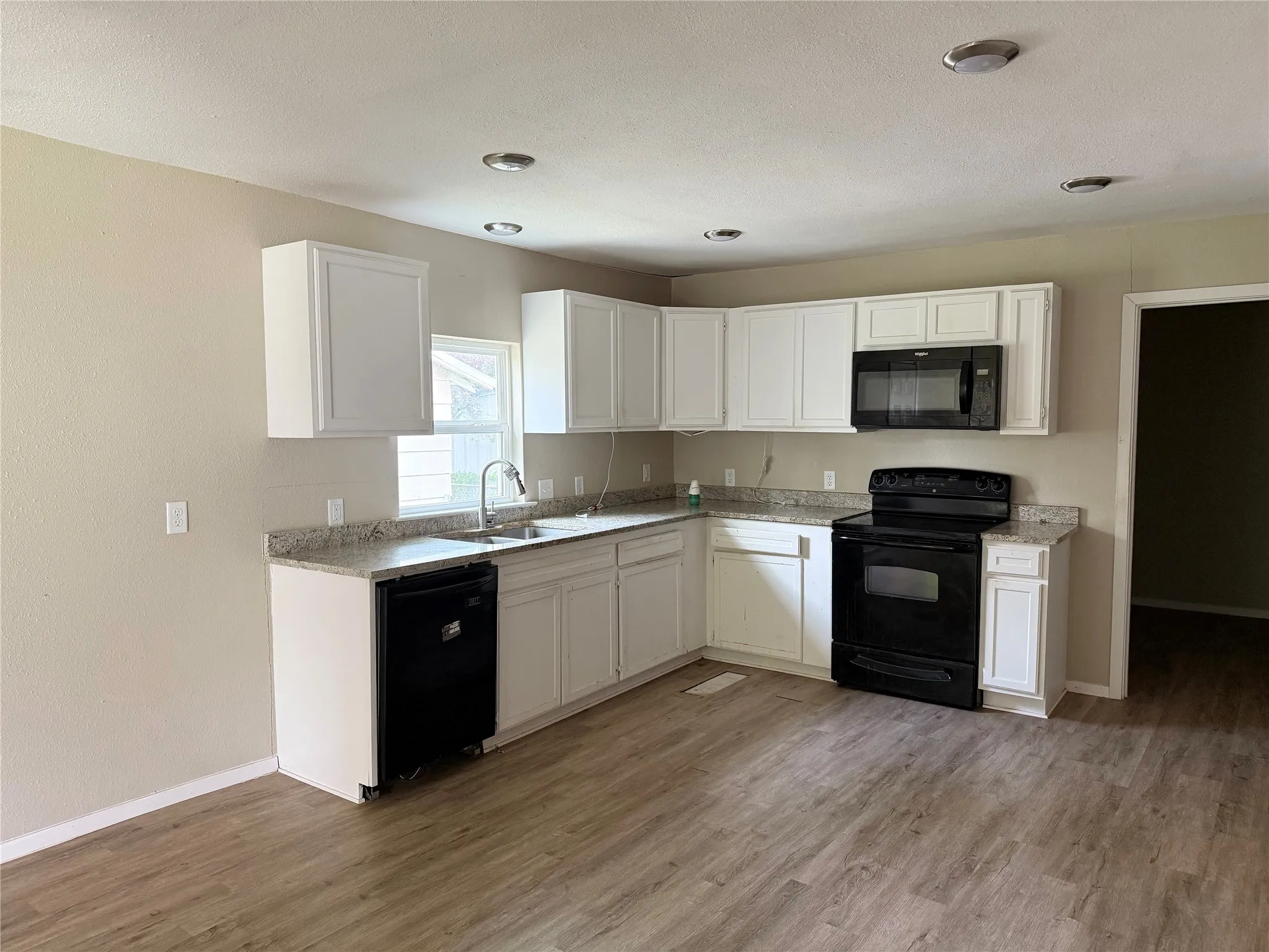 Kitchen with wood-finish flooring, white cabinetry, a black appliance suite, and light-toned countertops