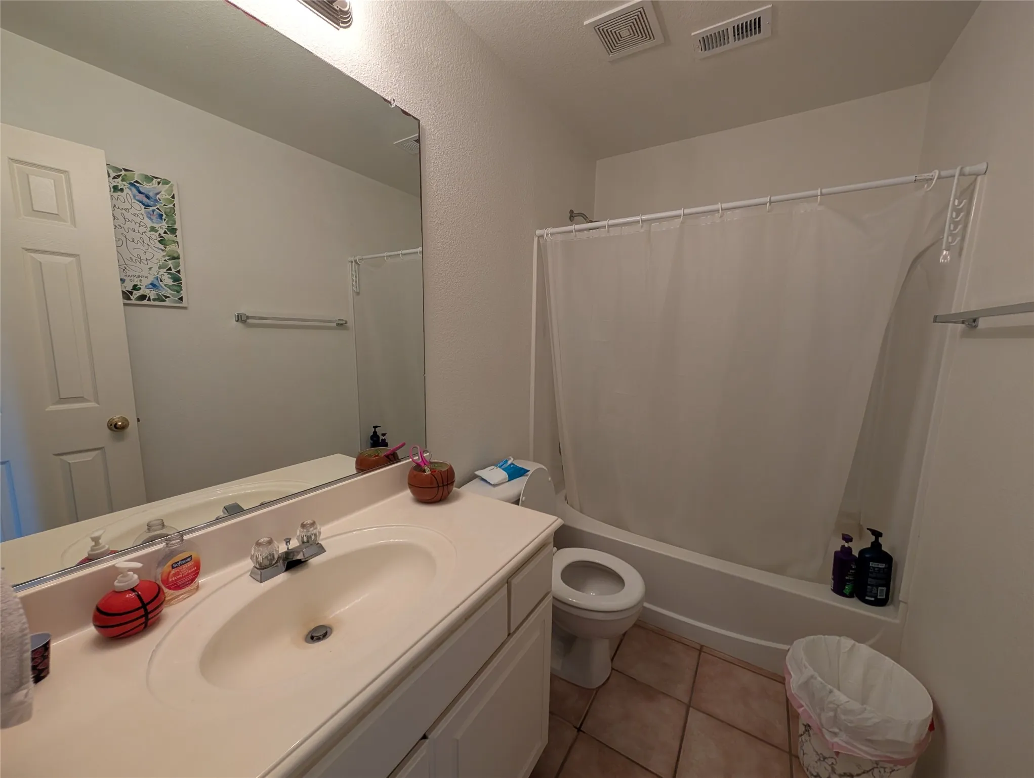 Bathroom featuring a single vanity with an integrated sink, a rectangular mirror, a bathtub with a shower, and tile flooring