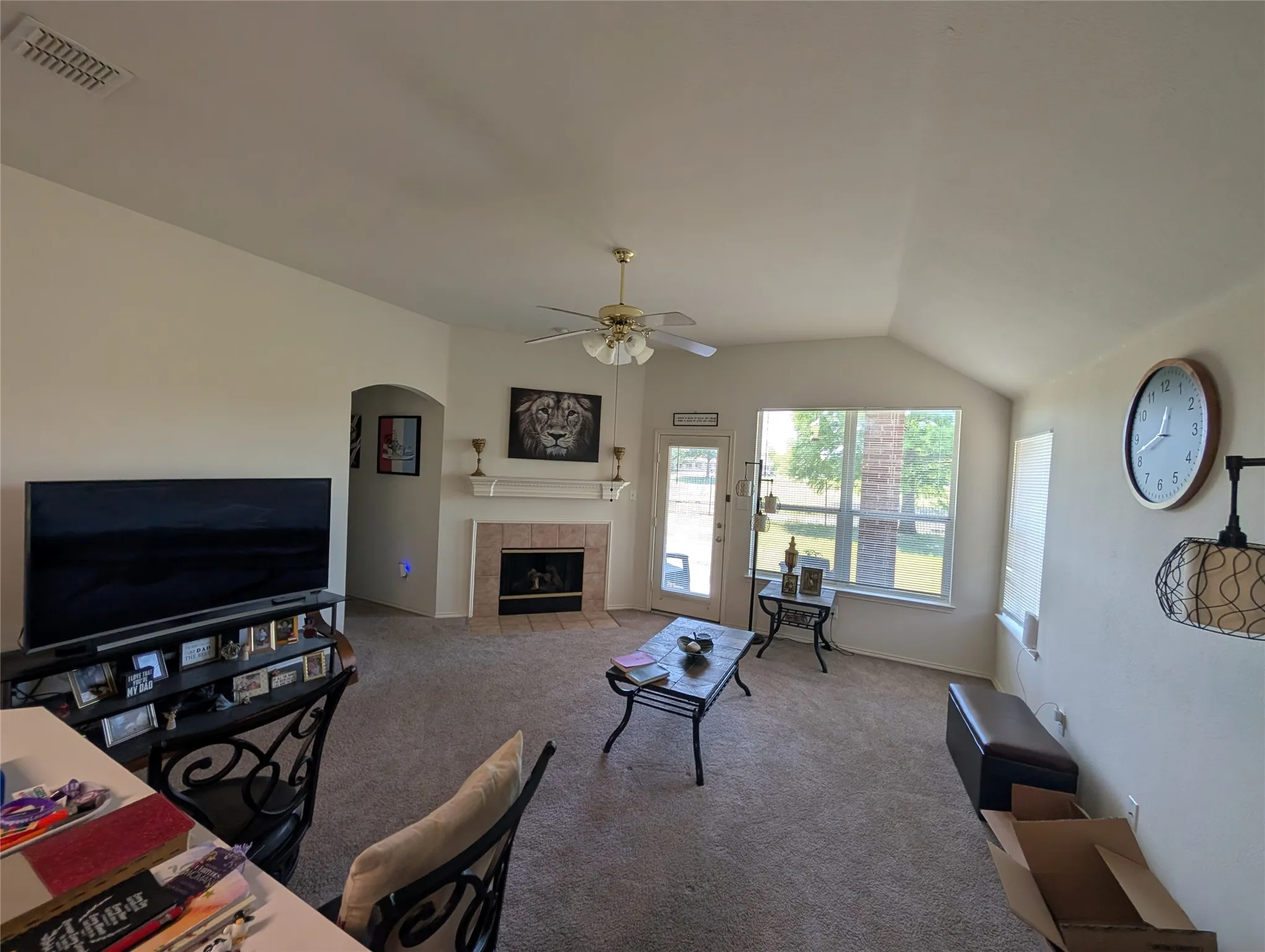 Vaulted ceiling living area featuring a tile-surround fireplace with a mantel, an arched entryway, a ceiling fan with integrated lighting, and carpet flooring