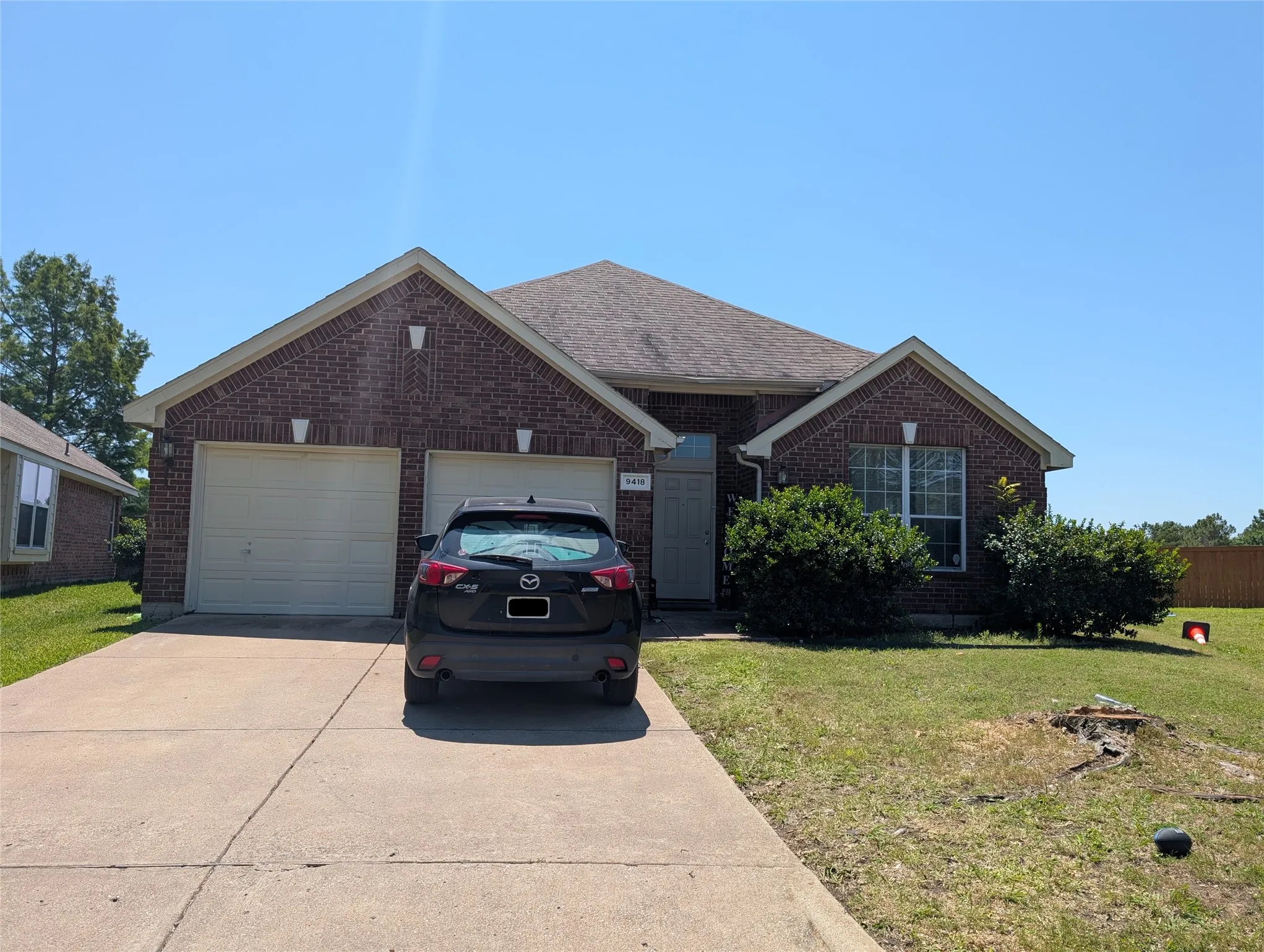 Brick facade home featuring a two-car garage, concrete driveway, and front lawn with established shrubbery