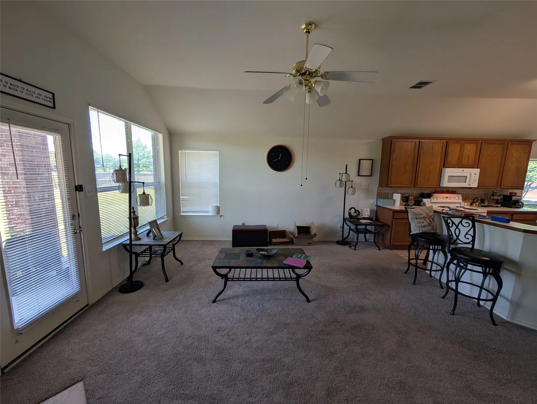 Carpeted living area with vaulted ceilings, a ceiling fan, and multiple windows providing natural light