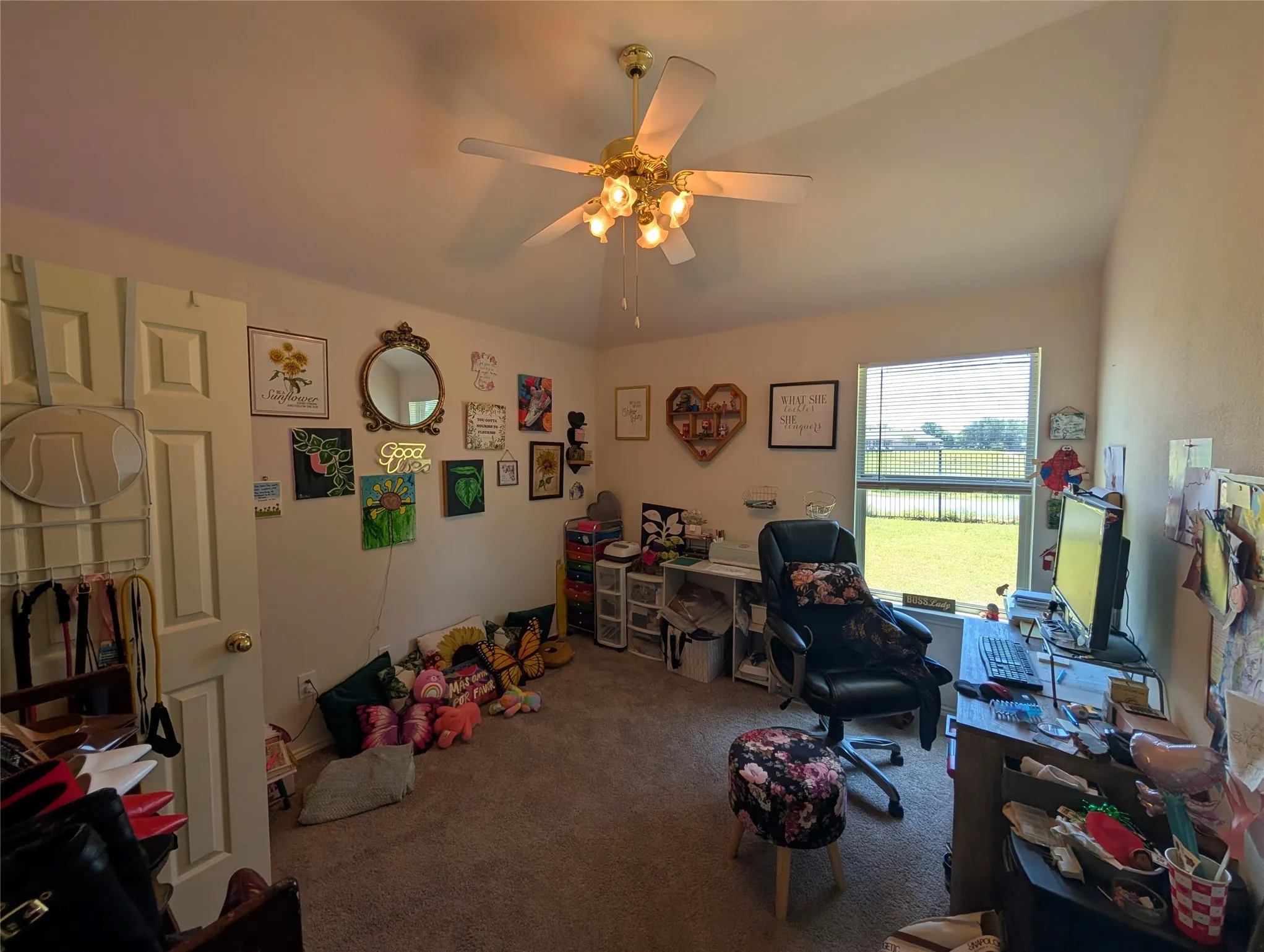 Carpeted room with a ceiling fan light fixture, white interior doors, and a window providing a green outdoor view
