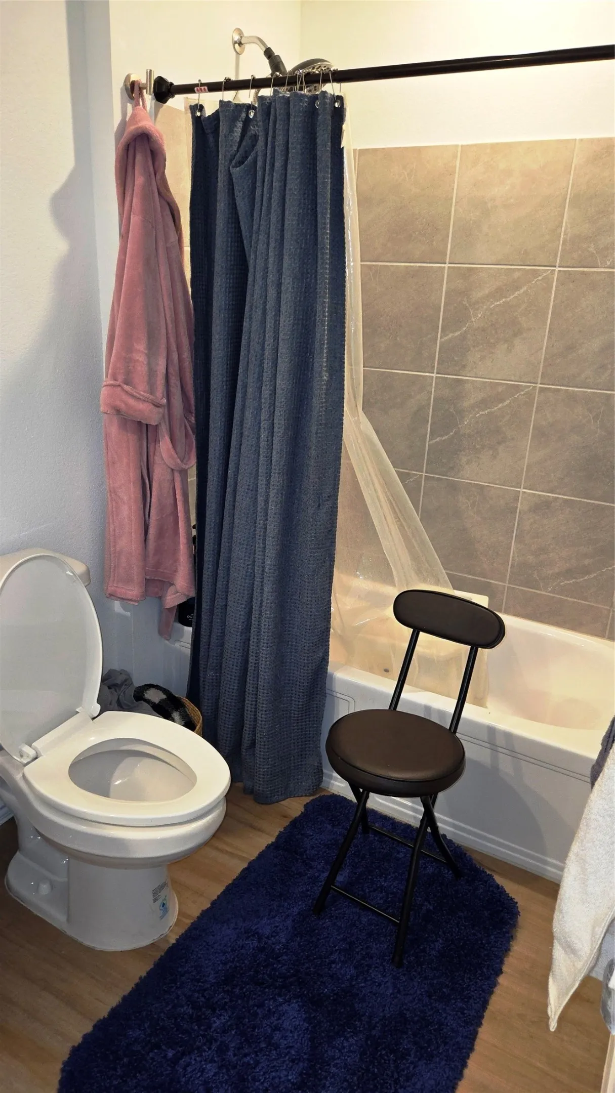 Bathroom featuring a bathtub with subway tile surround, white toilet, and wood-finish flooring