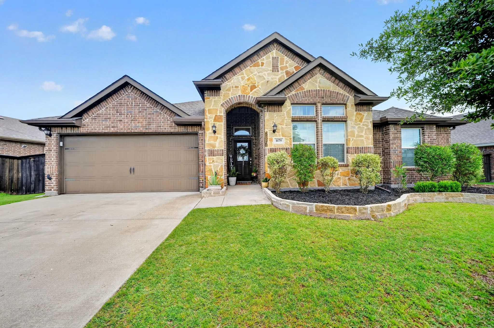 Stone and brick exterior featuring a multi-pane window, arched entryway, and integrated landscaping with stone borders