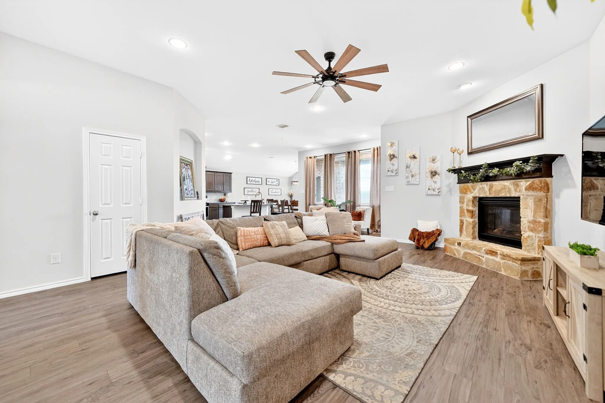 Spacious living area featuring wood-finish flooring, a stone fireplace, recessed lighting, and a ceiling fan