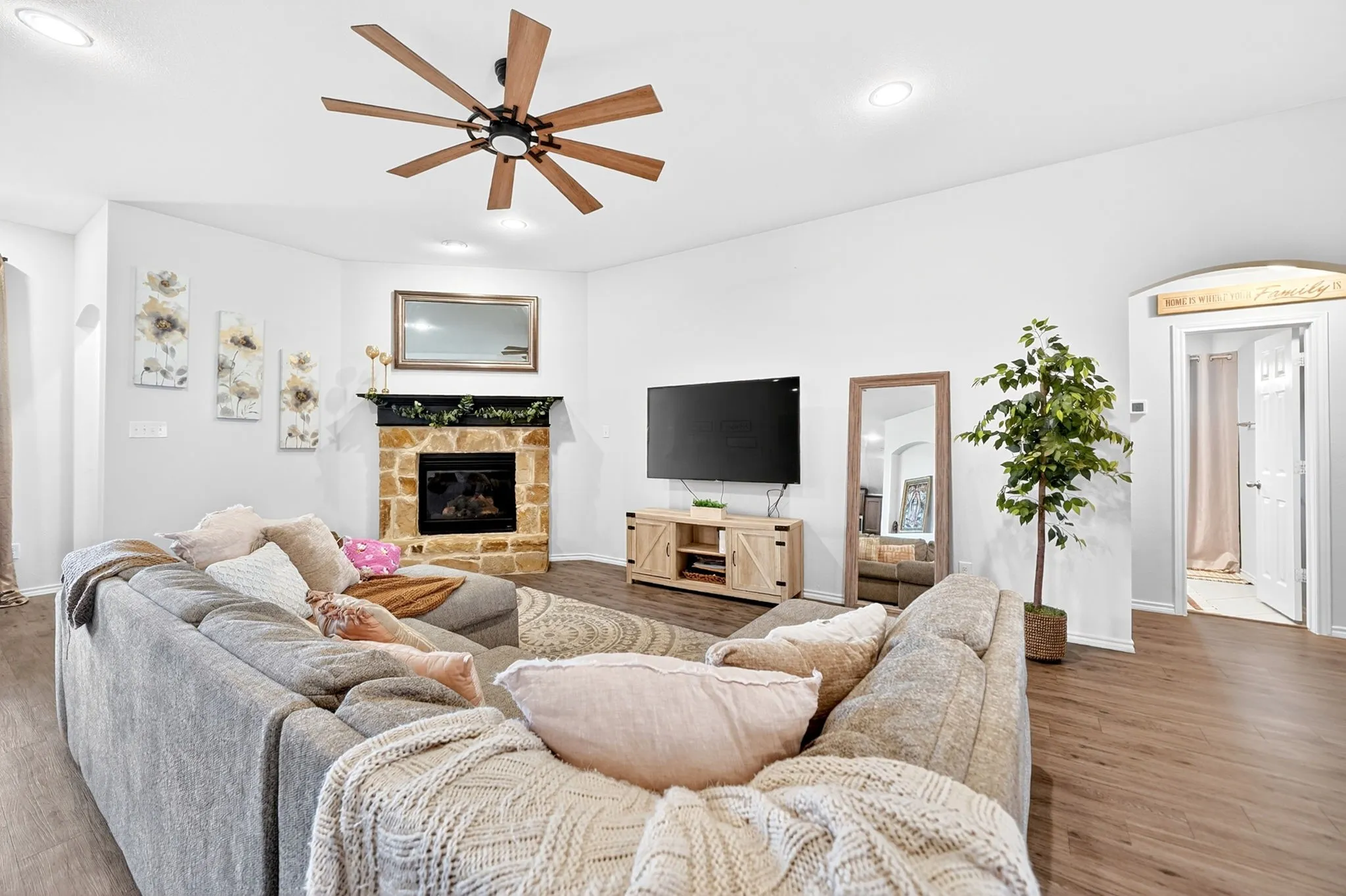 Living area featuring wood-finish flooring, a stone-clad fireplace with a black mantel, recessed lighting, and a multi-blade ceiling fan