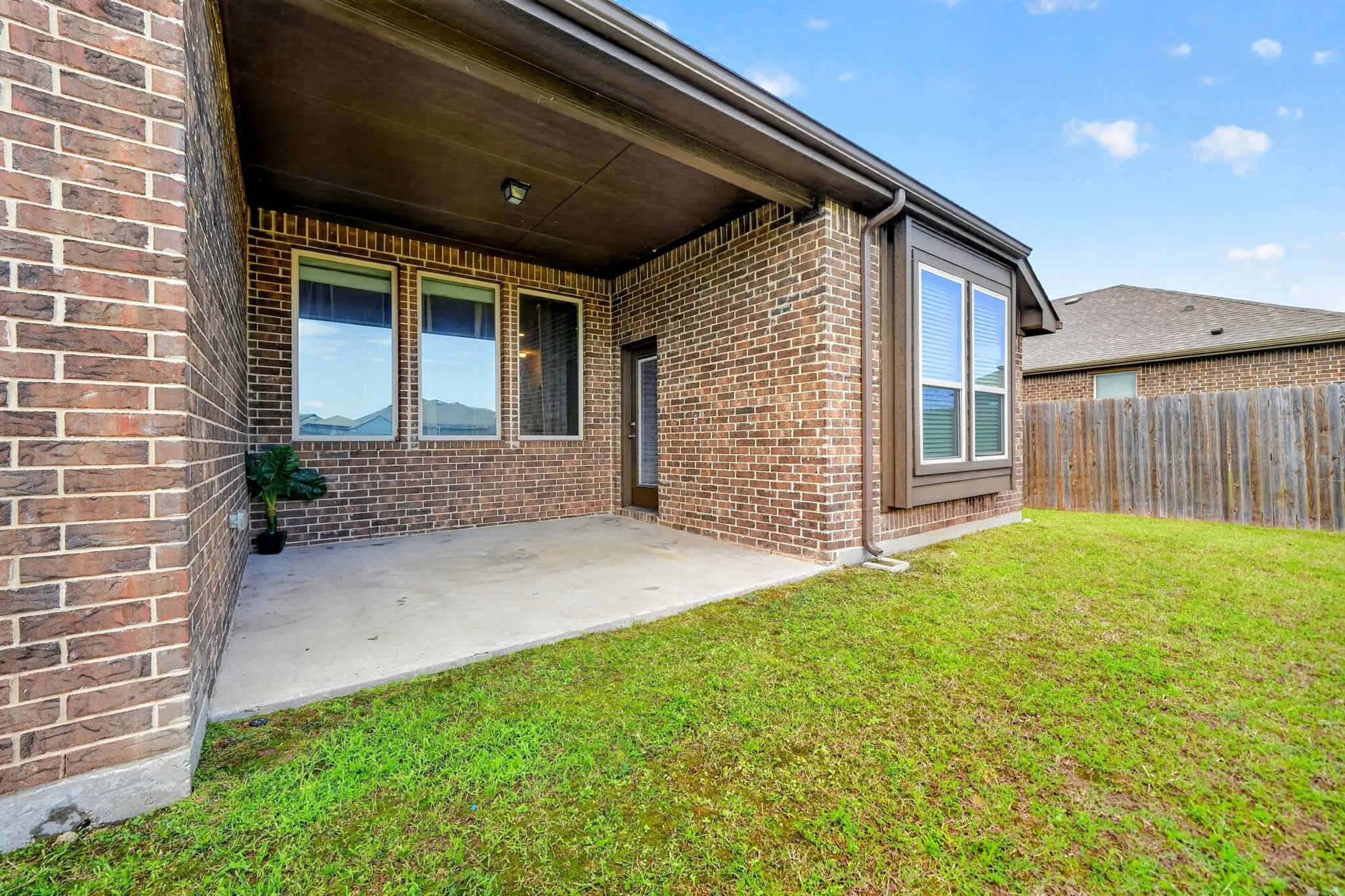 Covered patio with a concrete slab, brick exterior, and a manicured lawn
