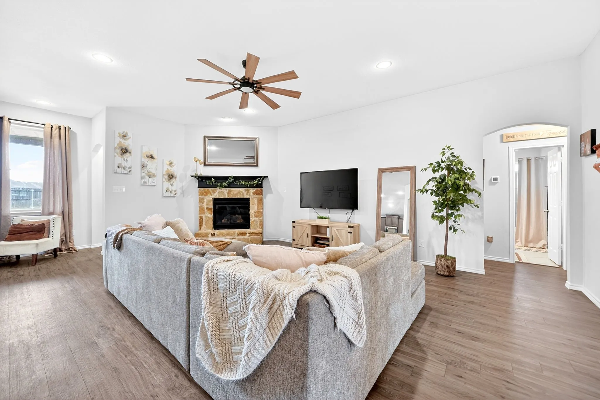 Spacious living area featuring wood-finish flooring and a stone-clad fireplace with a dark mantel