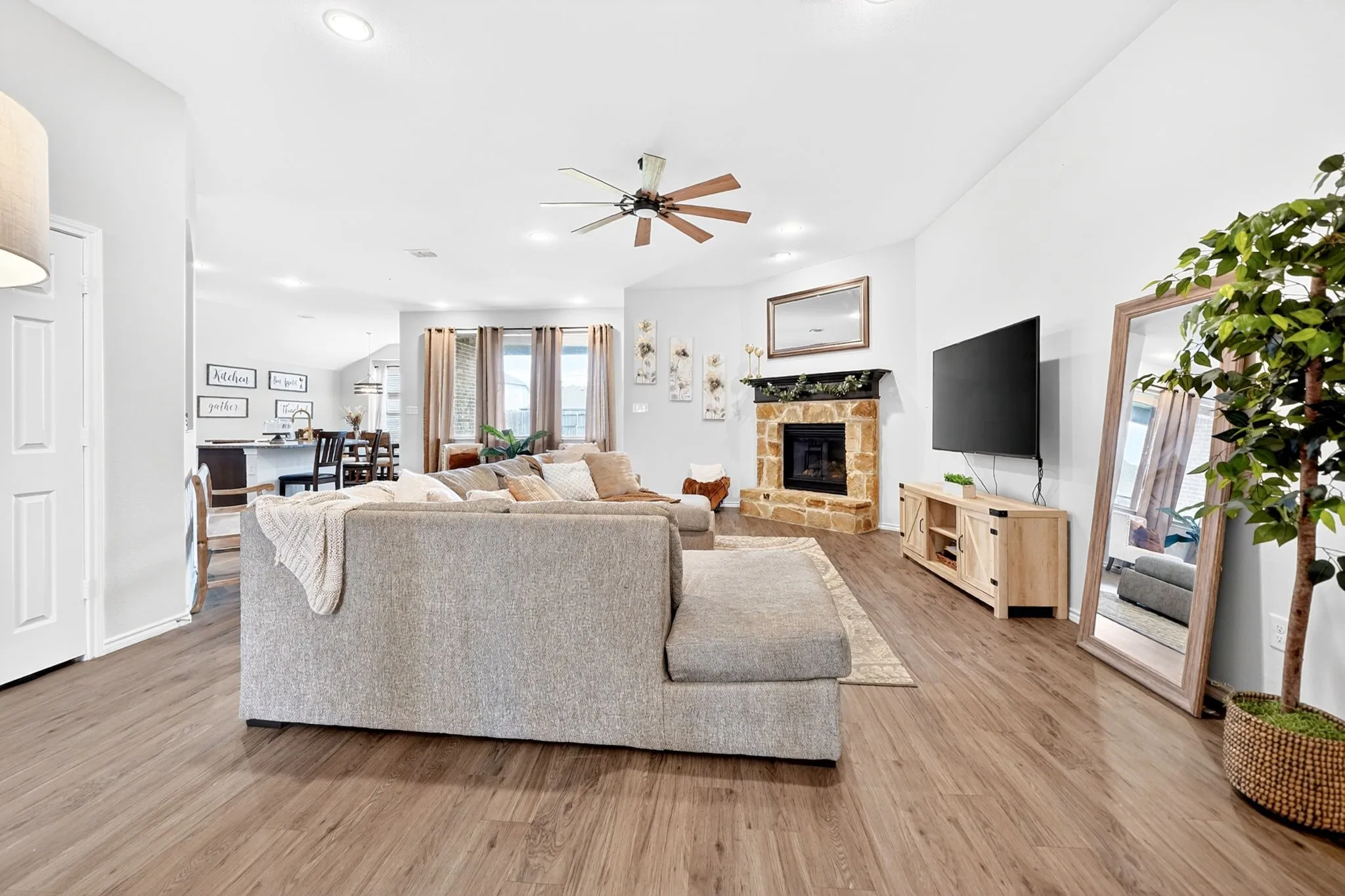 Spacious living area featuring wood-finish flooring, a stone fireplace with a dark wood mantel, recessed lighting, and a ceiling fan