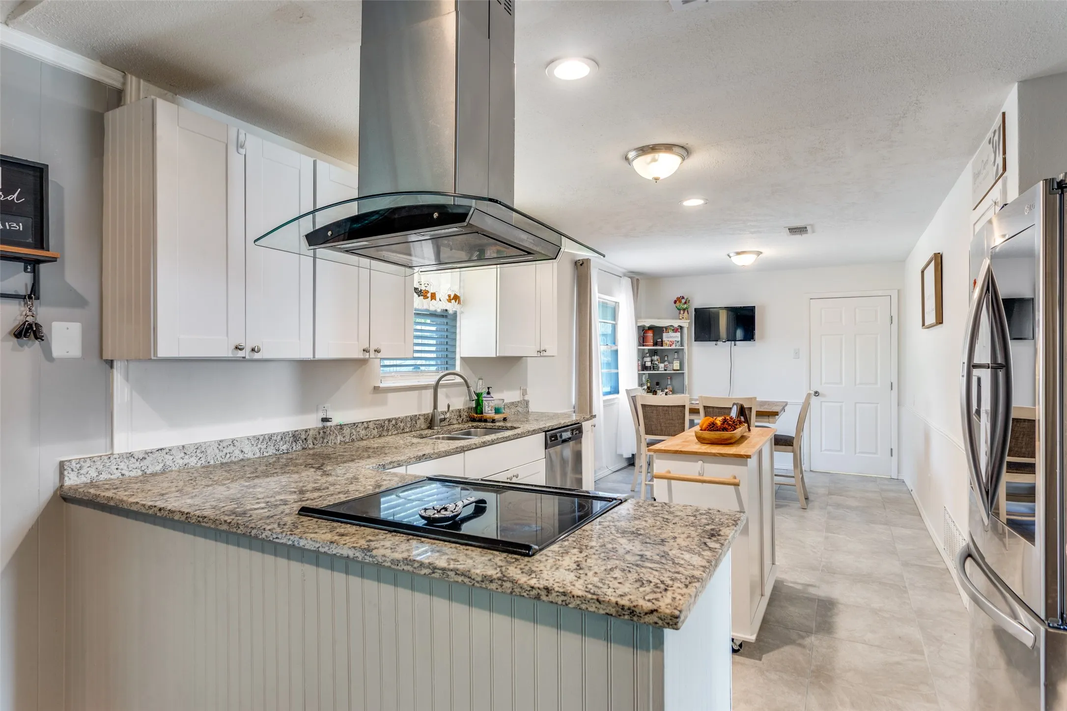 Kitchen featuring white cabinetry, granite countertops, stainless steel appliances, a range hood with glass canopy, and recessed lighting