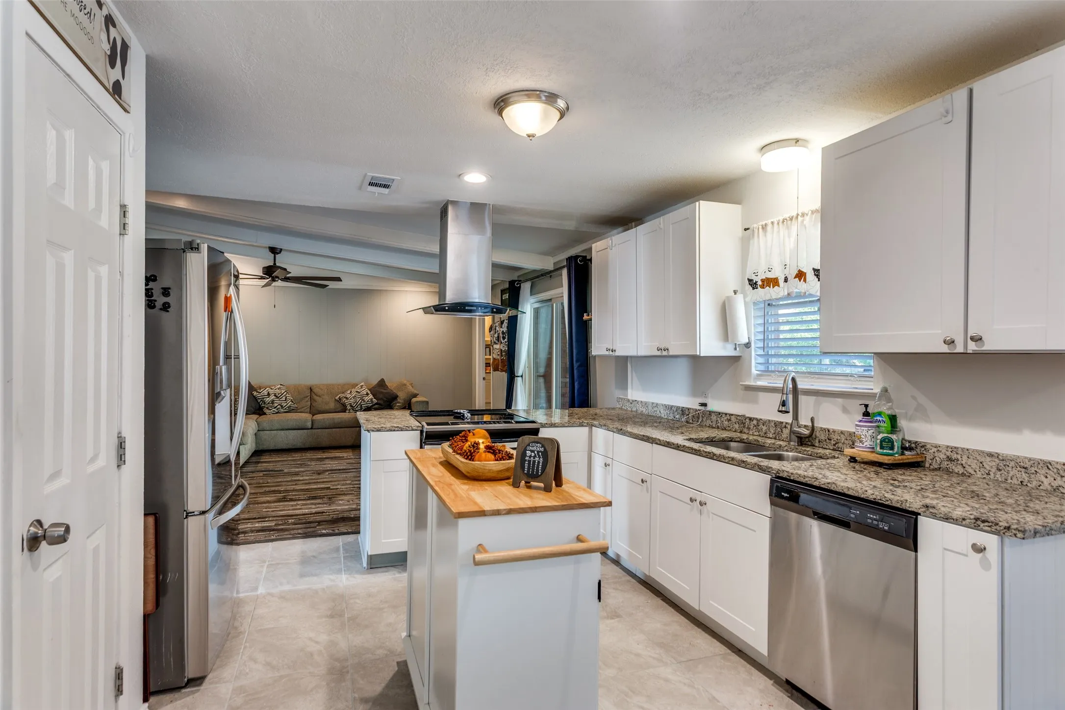 Modern kitchen featuring white cabinetry, light granite-style countertops, stainless steel appliances, a center island with a butcher block top, and tile flooring