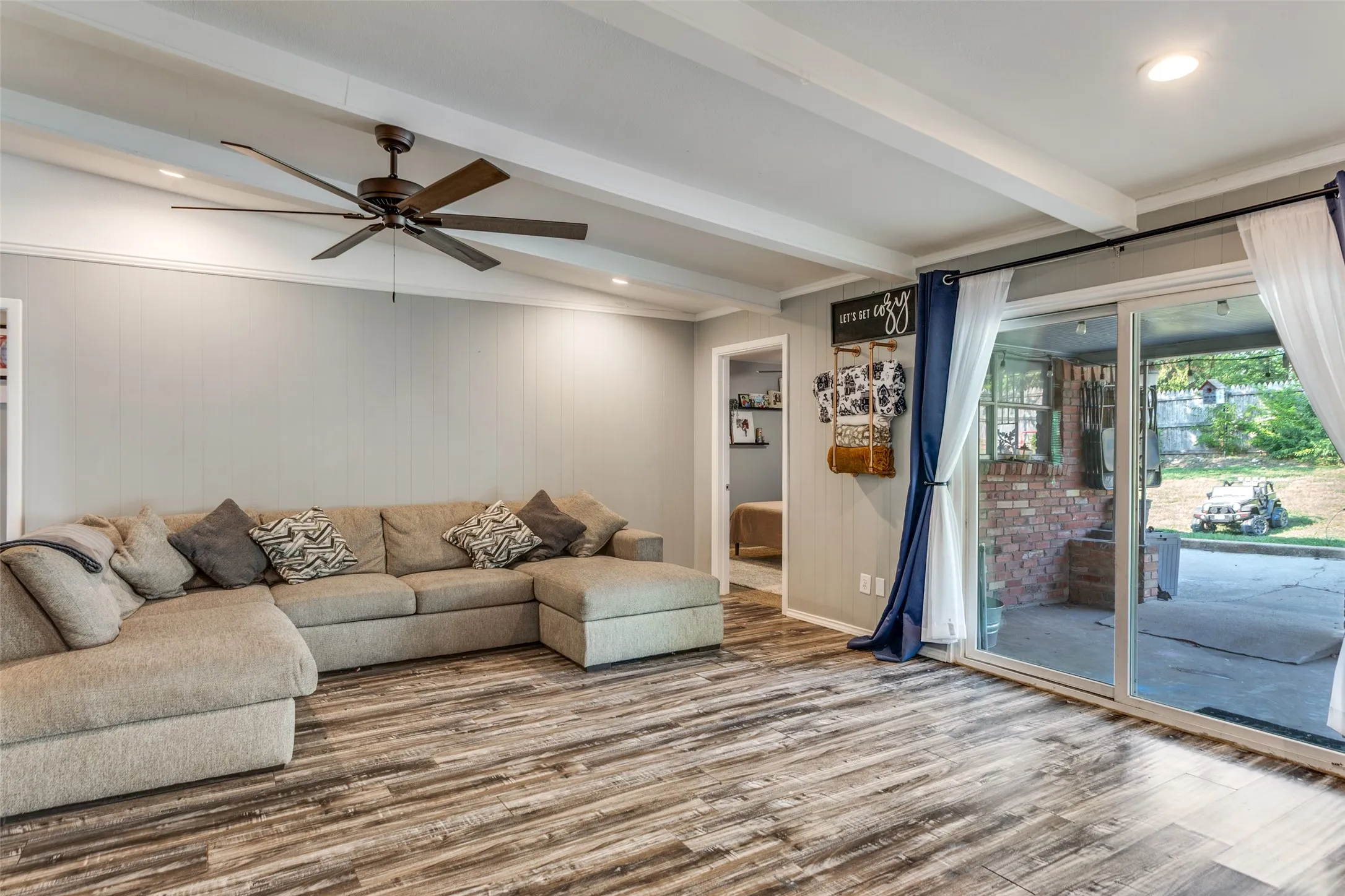 Spacious living area featuring wood-finish flooring, exposed ceiling beams, recessed lighting, and a ceiling fan