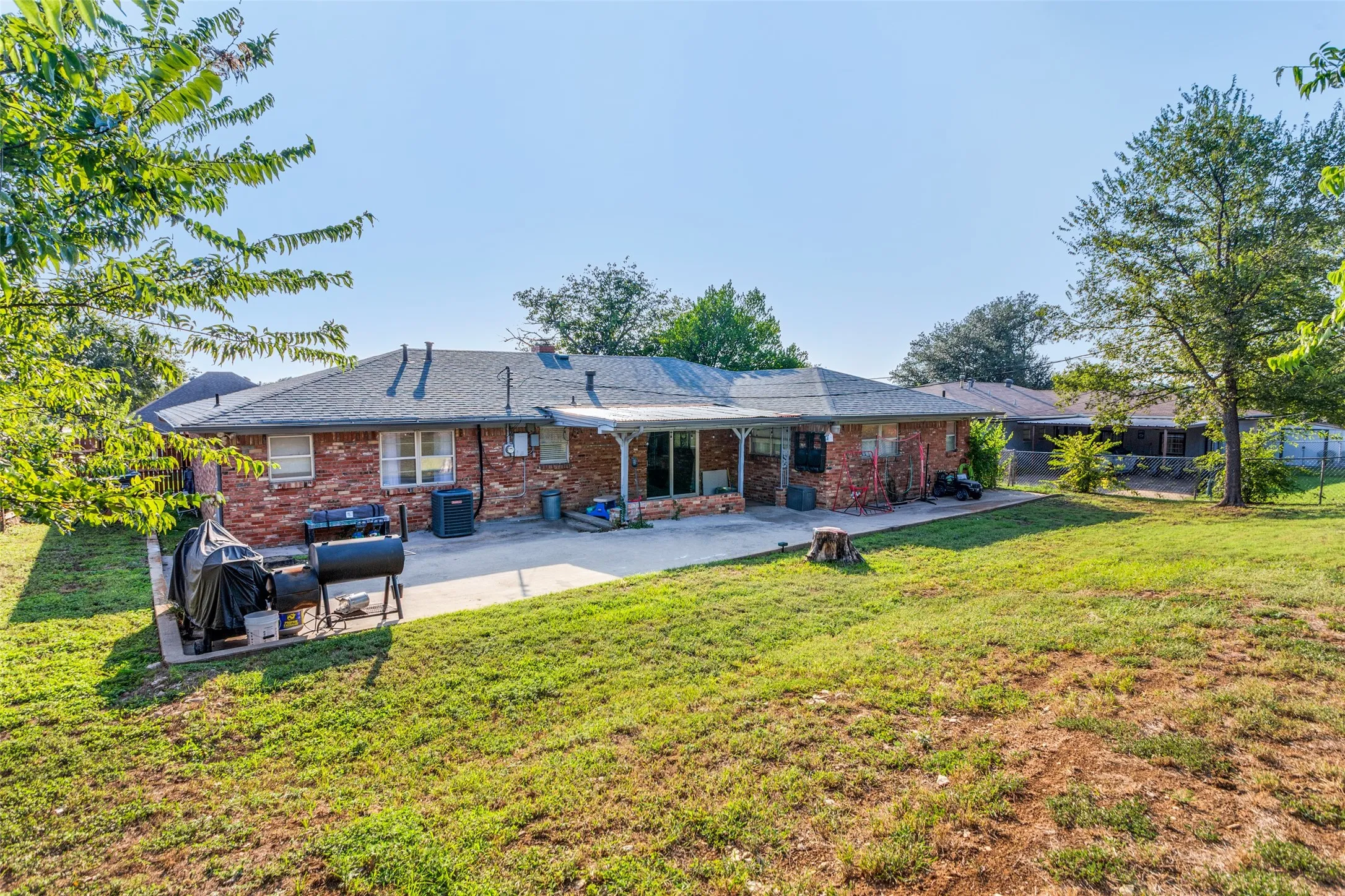 Spacious backyard featuring an extensive concrete patio, mature trees, and a brick exterior