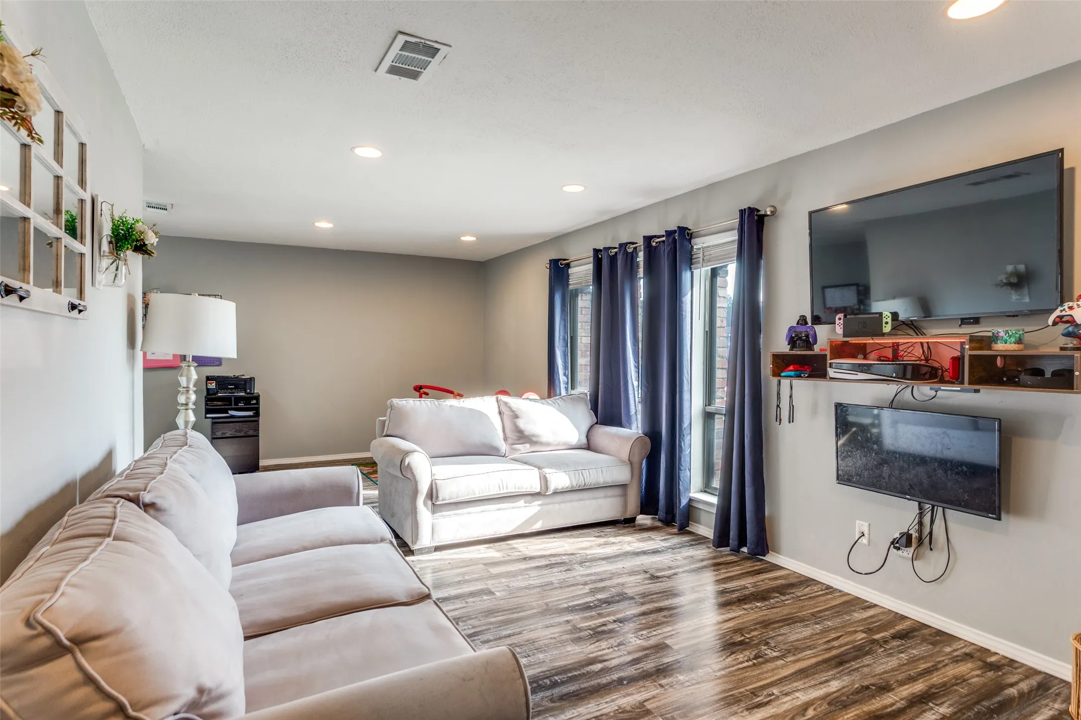 Living area featuring wood-finish flooring, recessed lighting, and multiple windows with vertical blinds