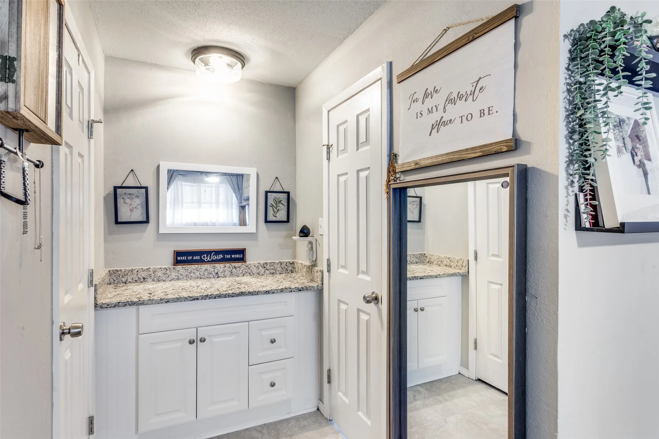 Vanity area featuring a granite-look countertop, white cabinetry with silver hardware, and a white framed wall mirror