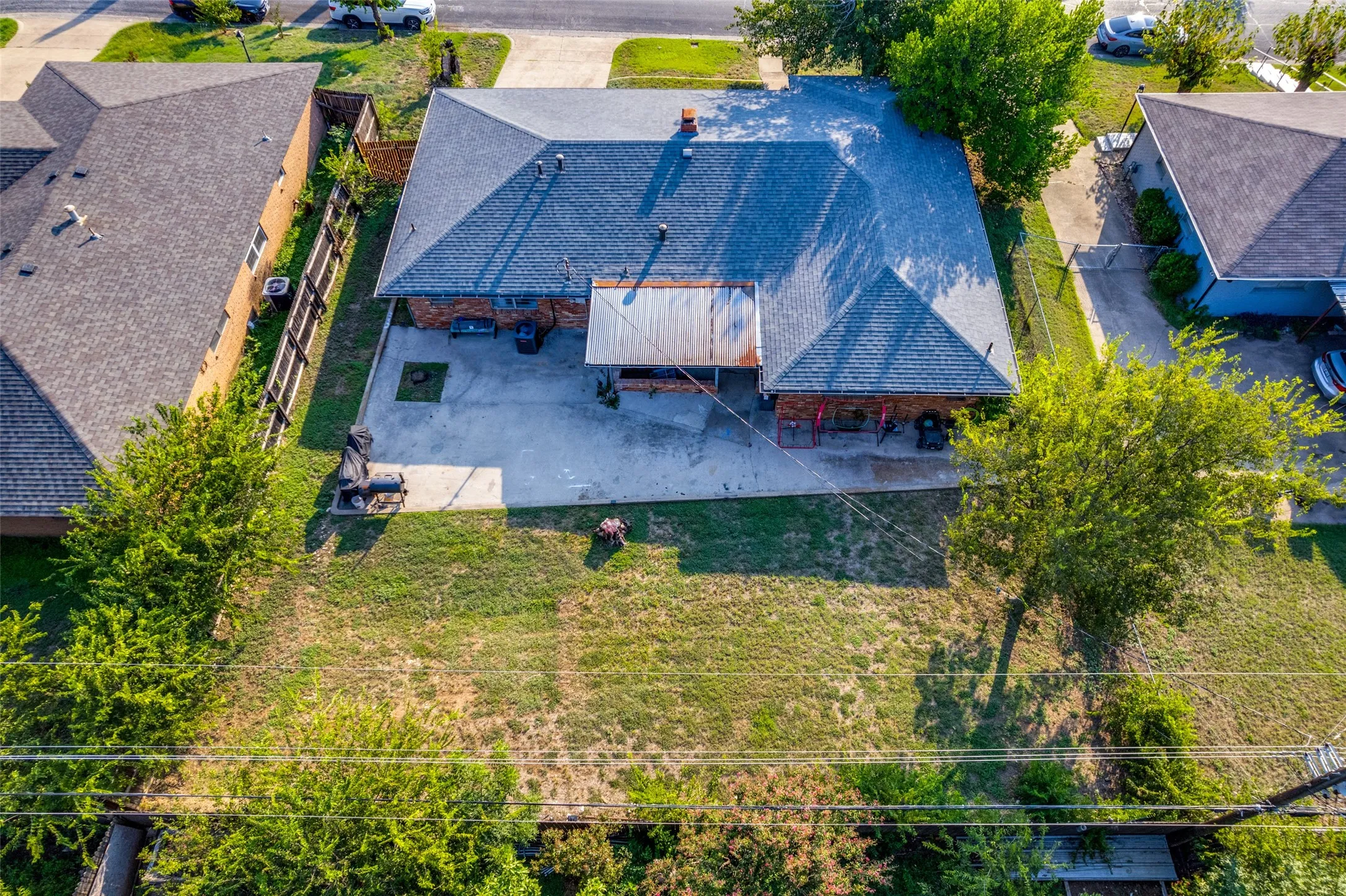 Asphalt shingle roofing over a brick exterior, featuring a concrete patio and a sloped backyard with mature trees