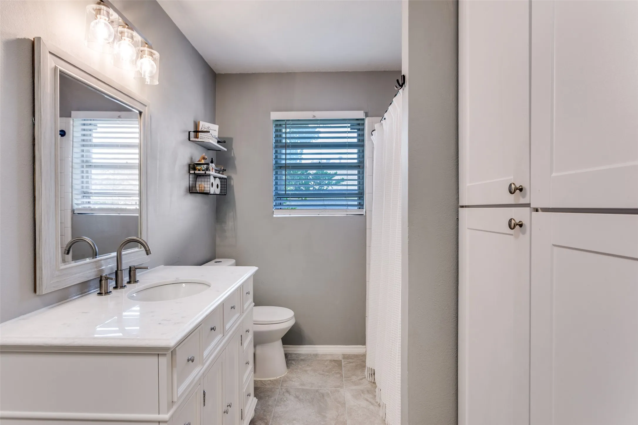 Bathroom featuring a single vanity with a white countertop, undermount sink, and brushed nickel faucet