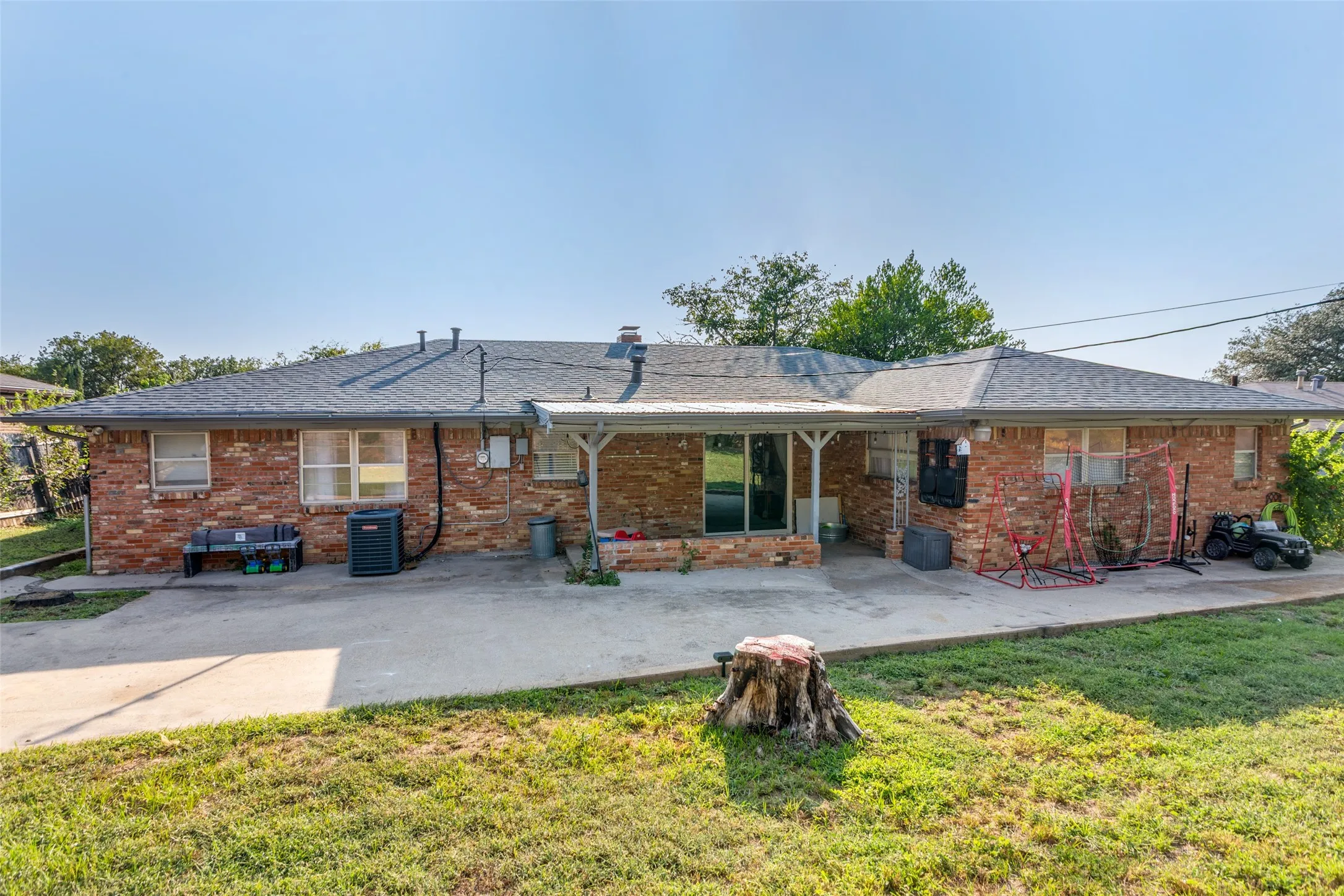 Rear exterior showcasing a brick facade, covered patio area, and a large concrete slab