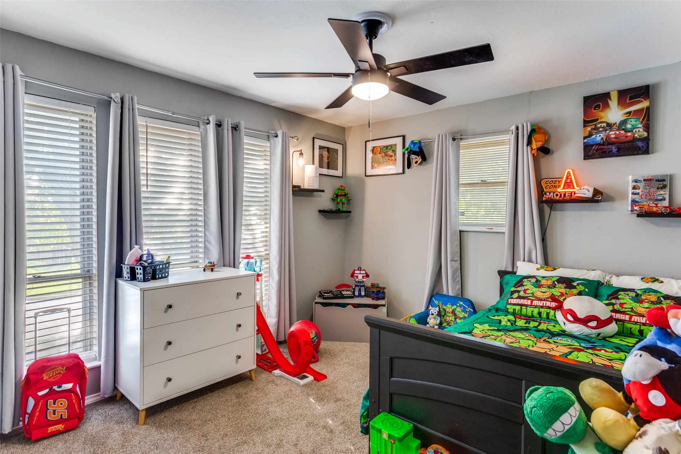 Carpeted room featuring a ceiling fan with integrated lighting, multiple windows with blinds