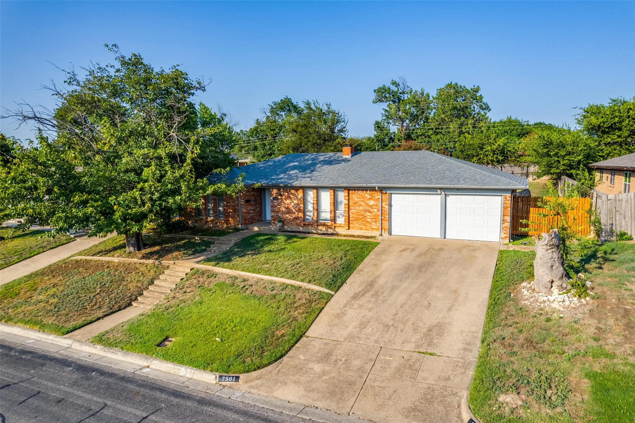 Brick exterior featuring a two-car garage, a concrete driveway, and a shingle roof