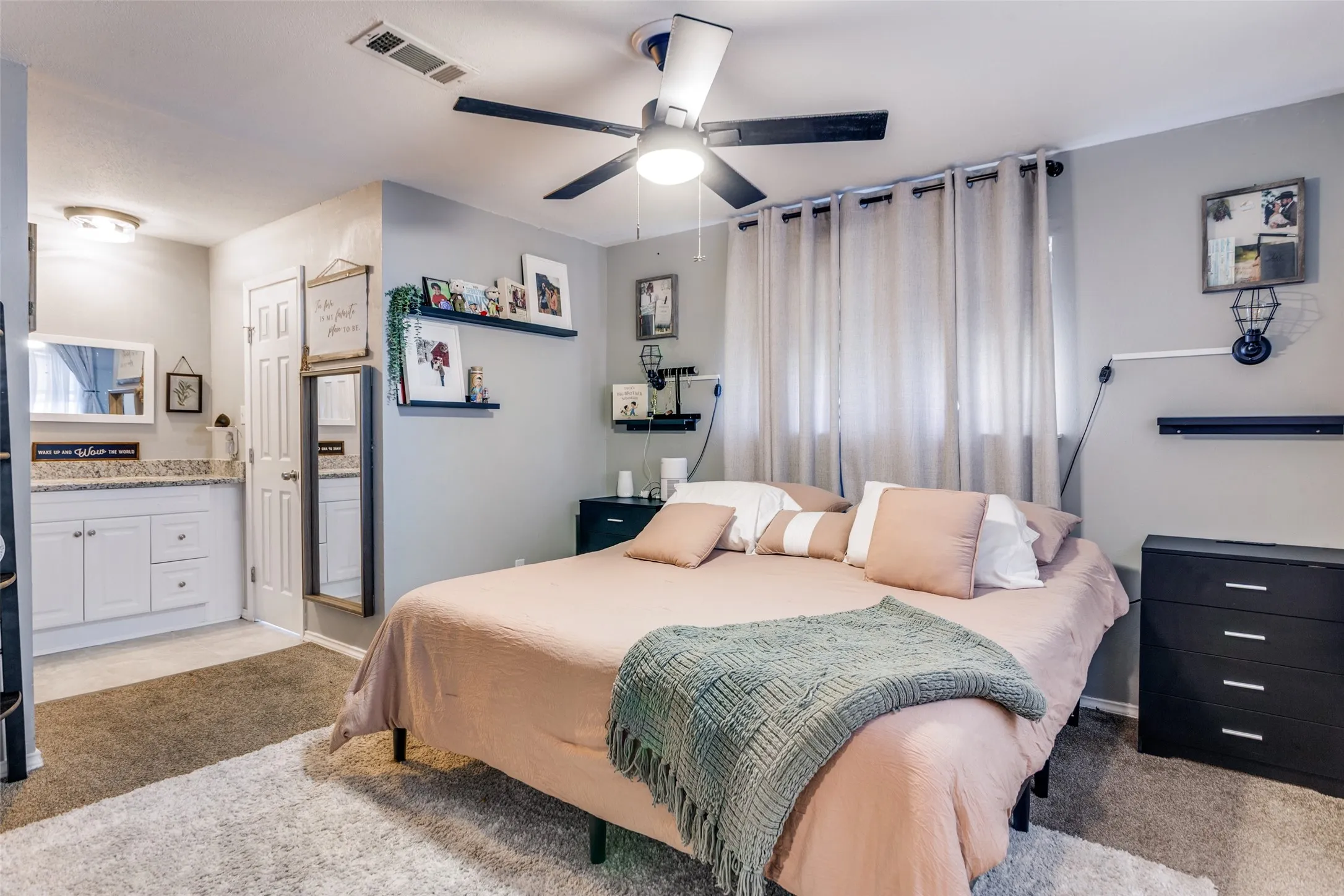Comfortable bedroom featuring a ceiling fan with integrated lighting, wall-mounted shelving, and window treatments