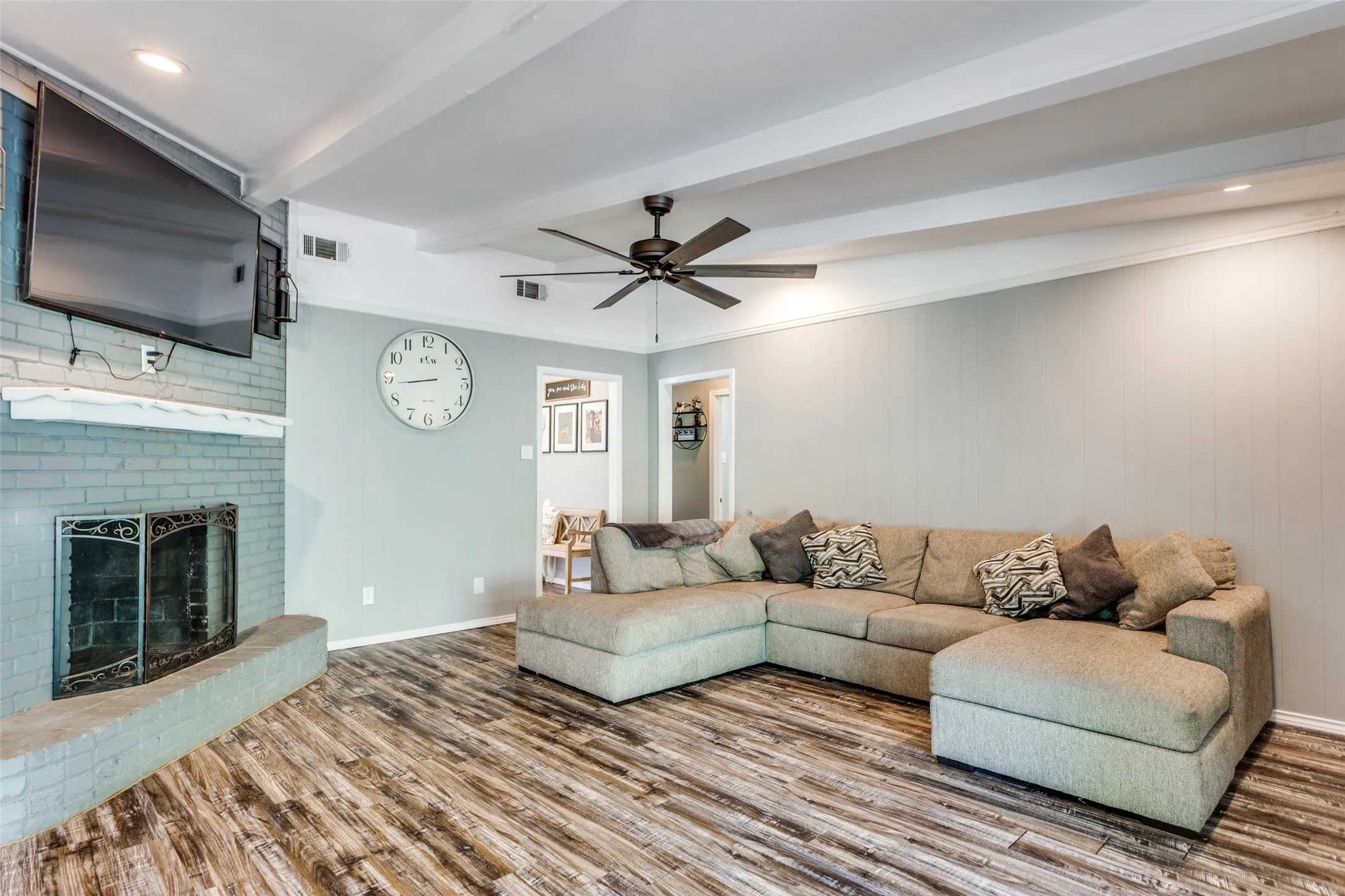 Living area featuring wood-finish flooring, a painted brick fireplace with a hearth, and a ceiling fan with integrated lighting