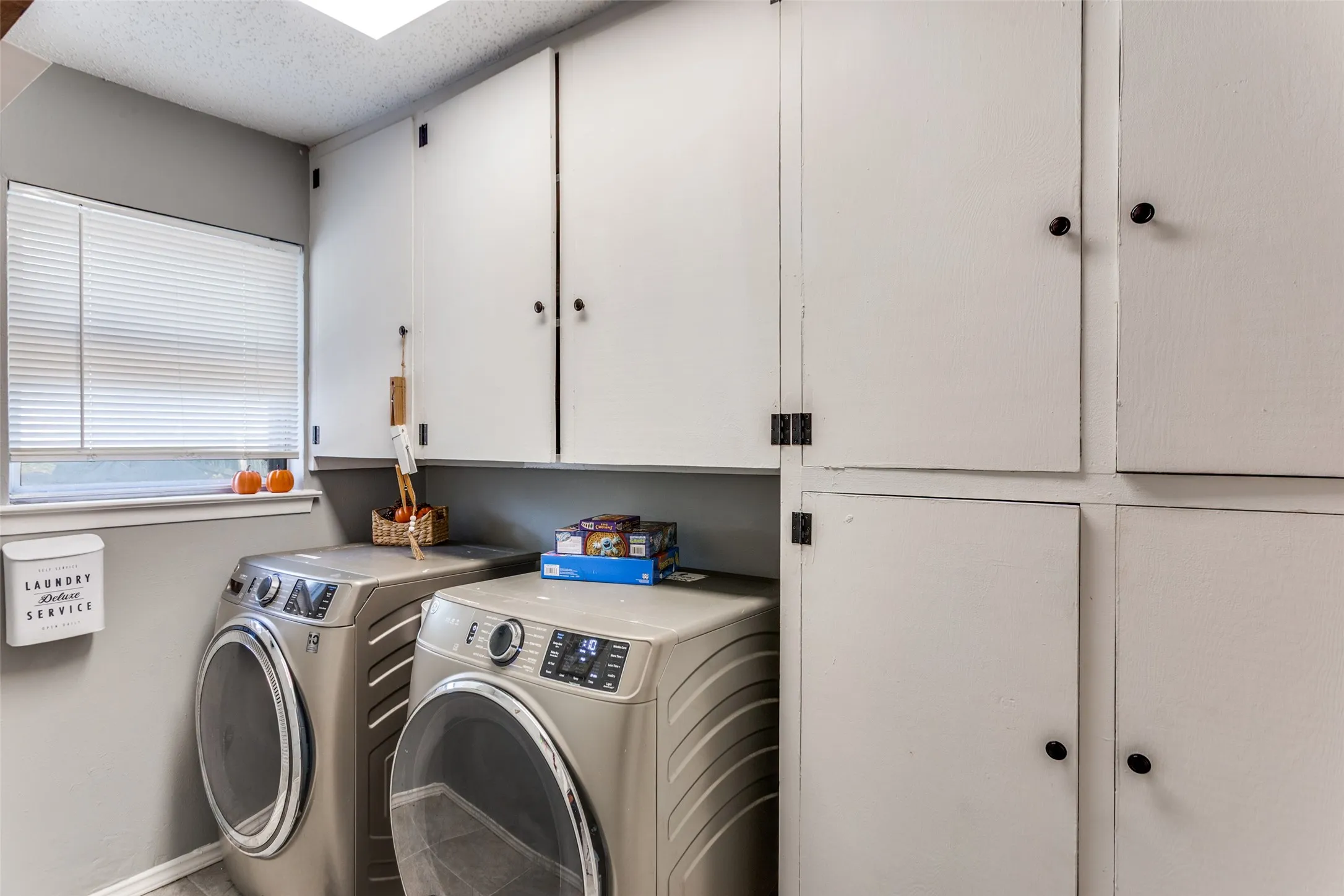 Laundry area featuring white cabinetry with black hardware, a window with blinds, and light gray wall paint