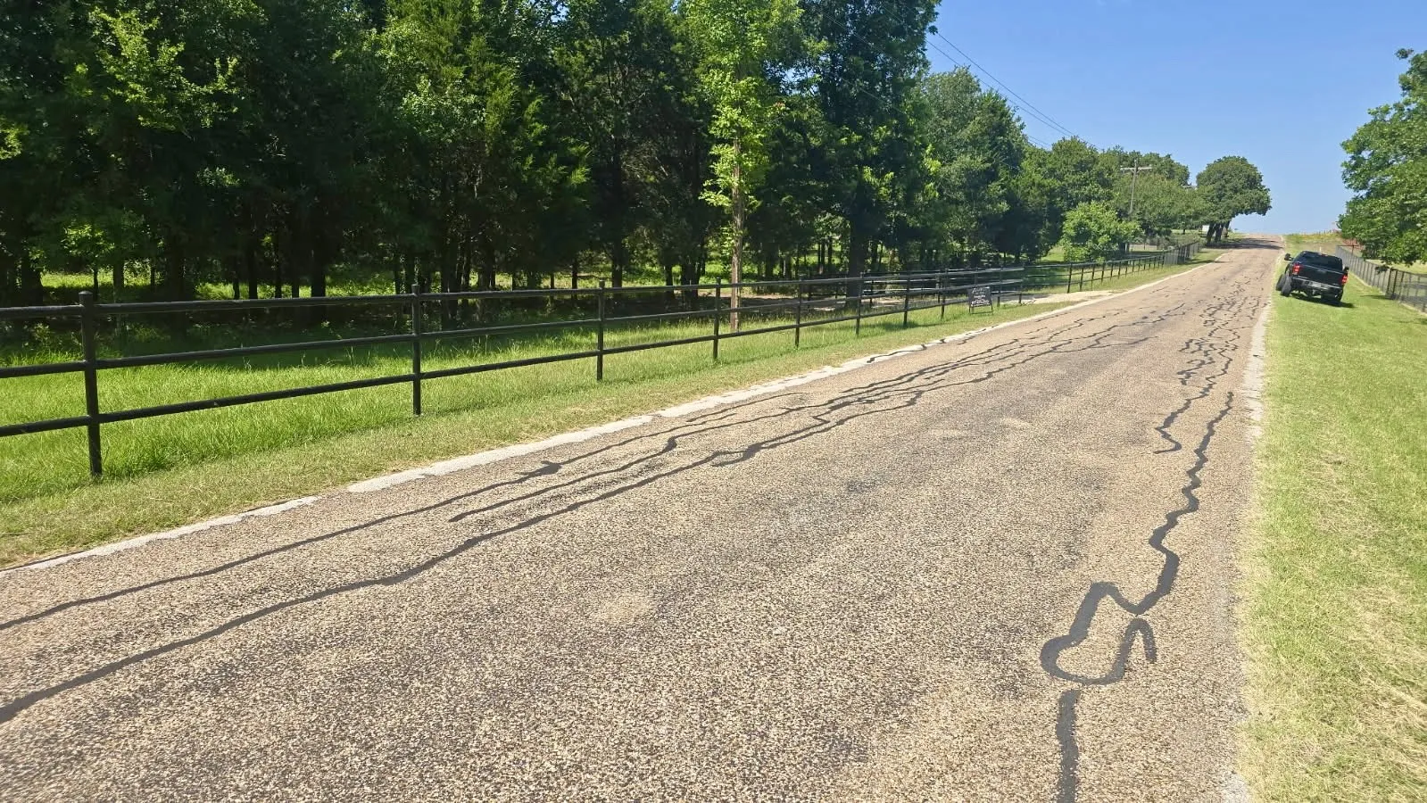 Gated property entrance with a paved driveway, expansive green lawn, and mature trees lining the perimeter