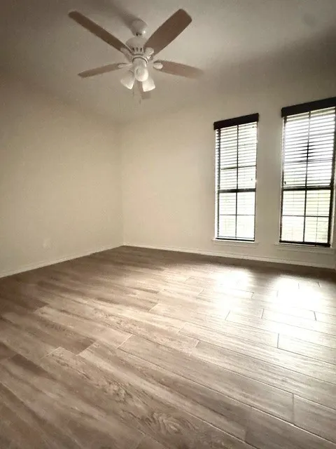 Neutral wall color, wood-finish flooring, two windows with blinds, and a ceiling fan with integrated lighting