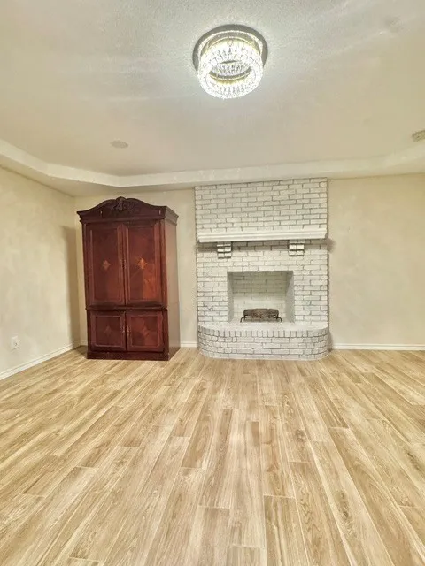 Wood-finish flooring throughout, tray ceiling, recessed lighting, and a white-painted brick fireplace