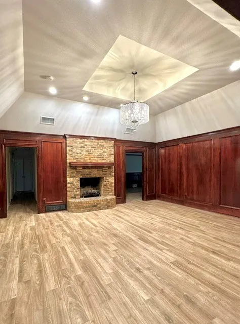 Recessed tray ceiling with a chandelier, vaulted ceiling, wood-finish flooring, brick fireplace, and wood paneling