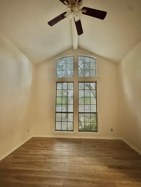 Vaulted ceiling with a central ceiling fan, expansive windows, arched upper windows, and wood-finish flooring