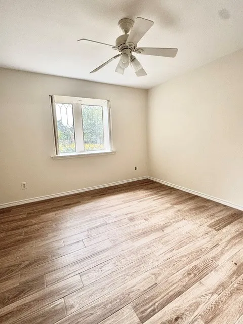 Wood-finish plank flooring with perimeter baseboards, a decorative leaded glass window, and a ceiling-mounted fan with integrated lighting