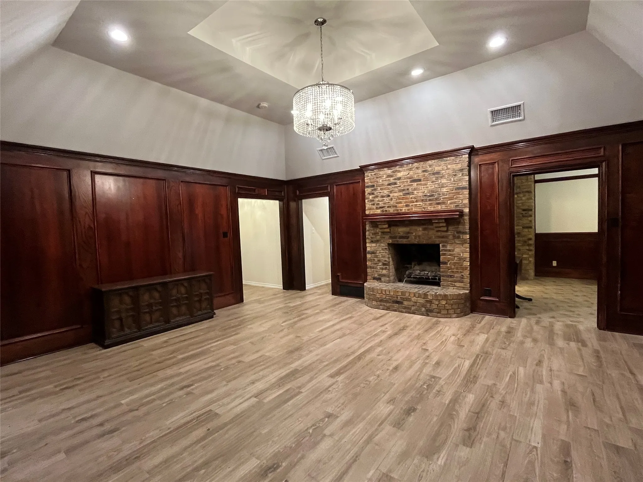 Living room with recessed tray ceiling, dazling chandelier, wood paneling, and fireplace