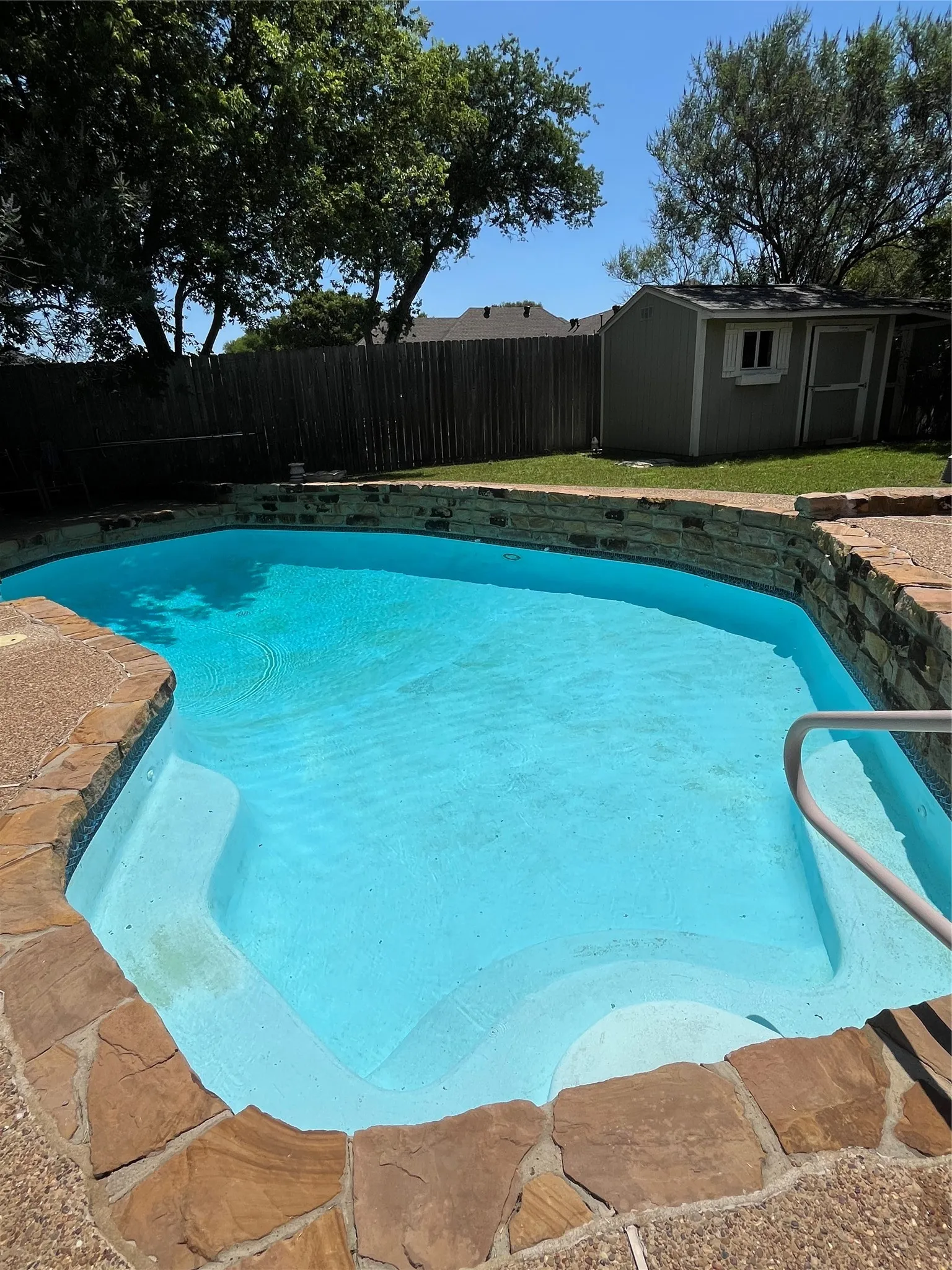Backyard swimming pool featuring stone coping, built-in steps, and a metal handrail