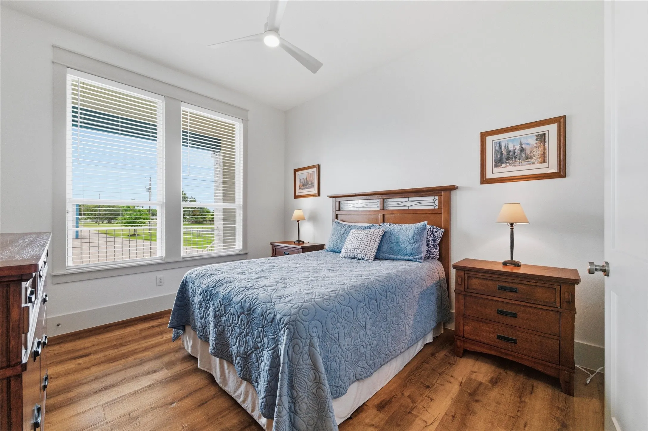 Secondary bedroom features large windows overlooking the surrounding property, neutral finishes, ceiling fan, and wood-look flooring throughout the space.