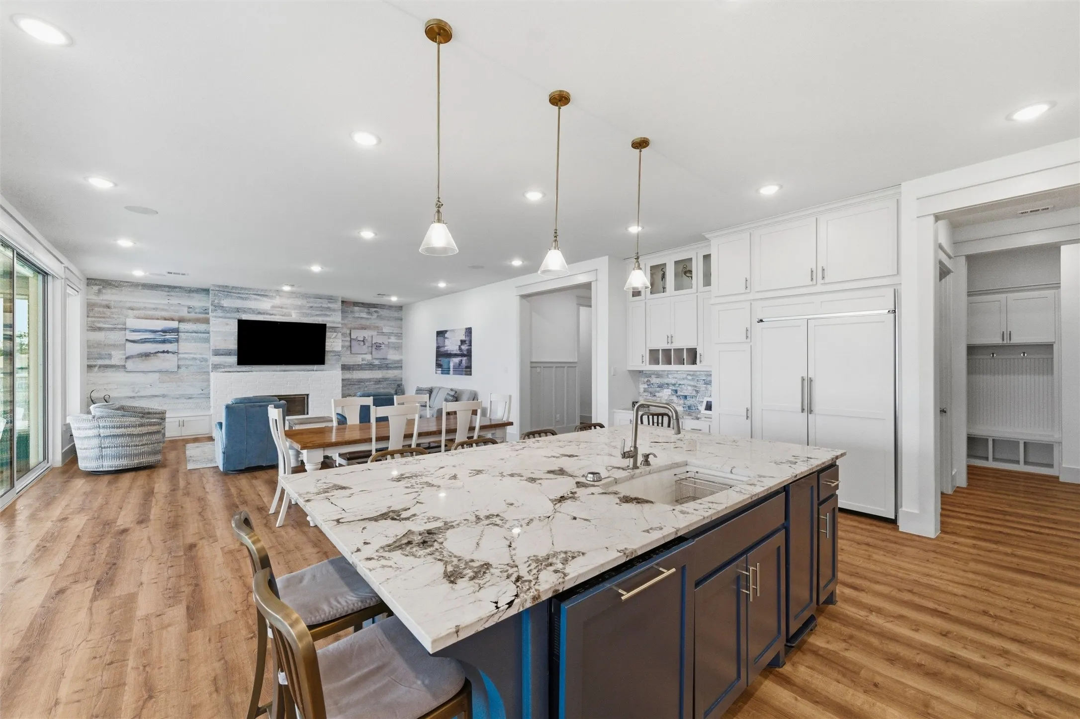 Kitchen showcases oversized center island with contrasting cabinetry, waterfall-style countertop edges, pendant lighting, and surrounding prep space. Cabinetry extends throughout the kitchen with integrated storage and stone countertop surfaces while maintaining open sightlines to the living area.