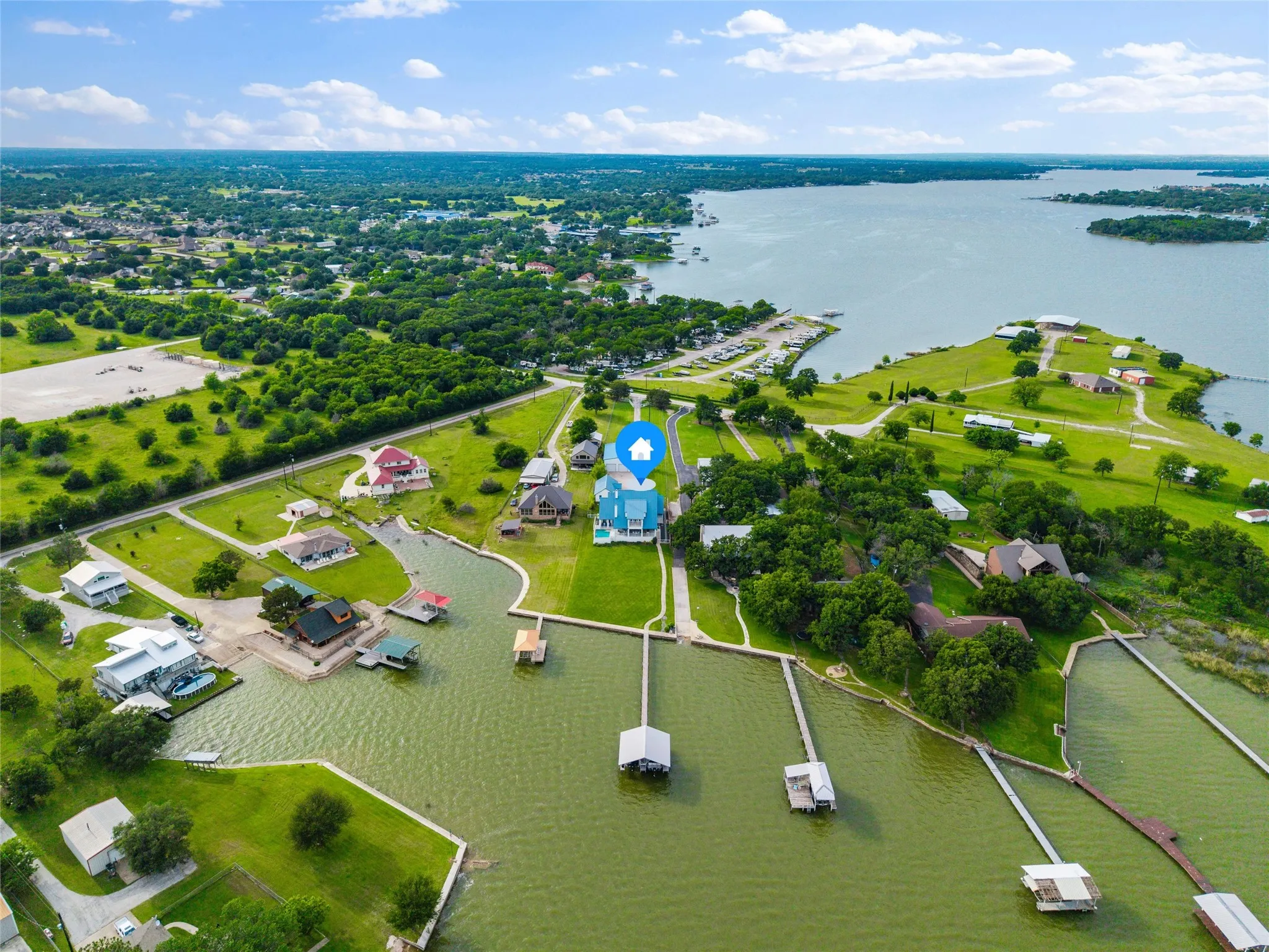 Aerial view highlights the waterfront positioning of the property with direct lake access, private dock, shoreline edging, surrounding lawn areas, and neighboring waterfront properties visible throughout the surrounding landscape.